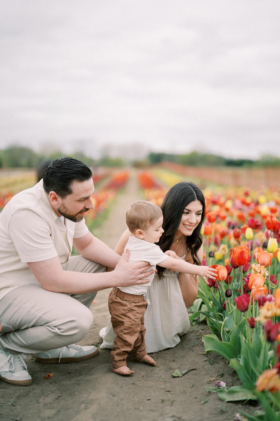 A family enjoying a day in a vibrant tulip field, with the child reaching out to touch the flowers.