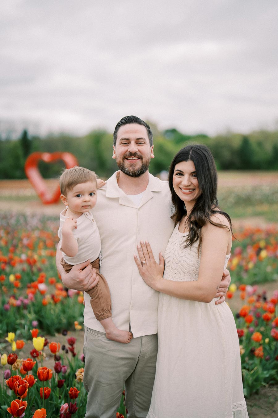 A family poses happily in a vibrant tulip field, with a large red heart sculpture in the background, symbolizing love and togetherness.