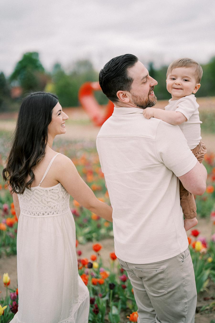 A family enjoys a day out in a colorful tulip field, with a red sculpture in the background, creating a picturesque scene.