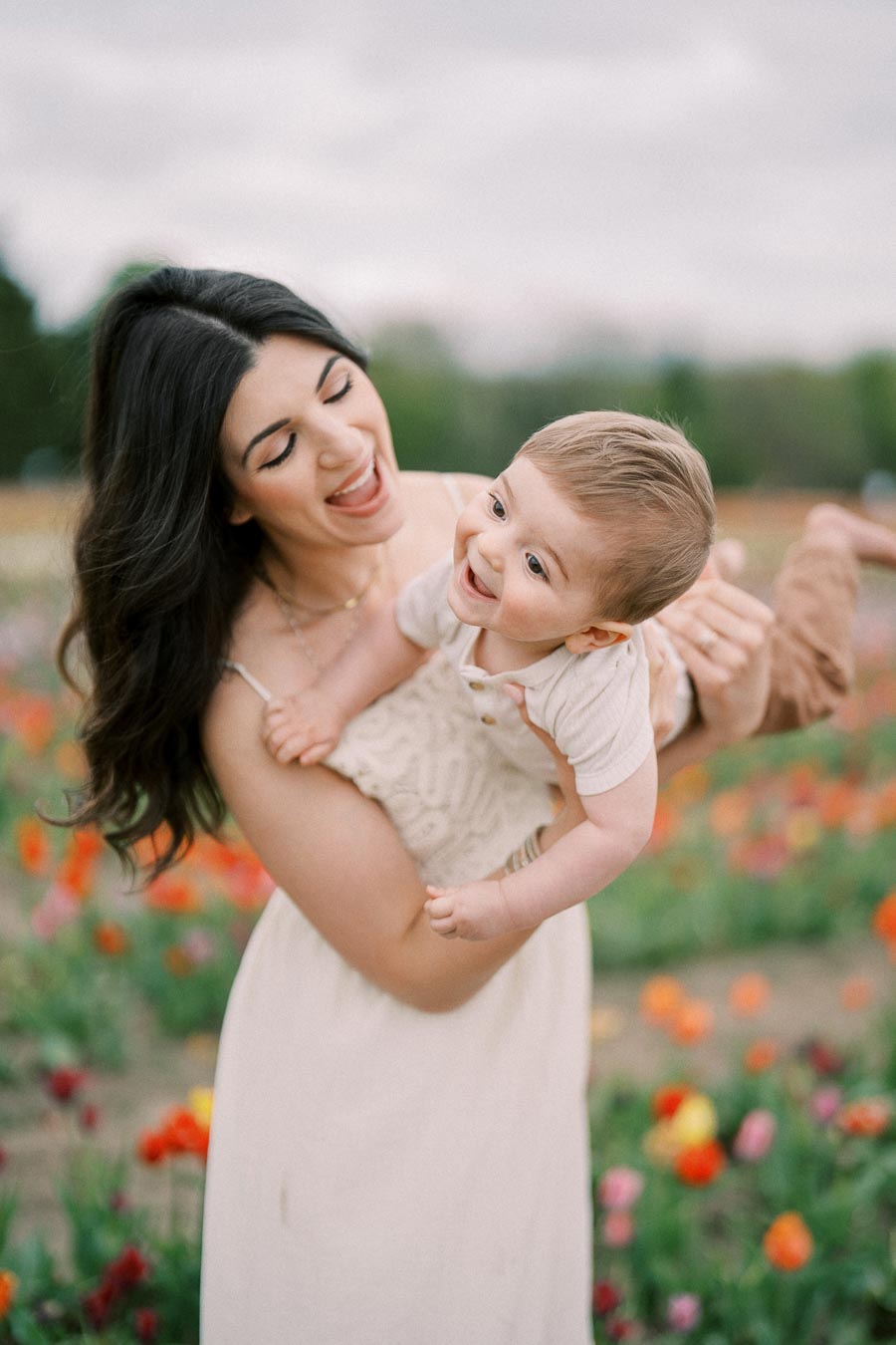 A joyful moment captured between a woman and a baby in a vibrant flower field.