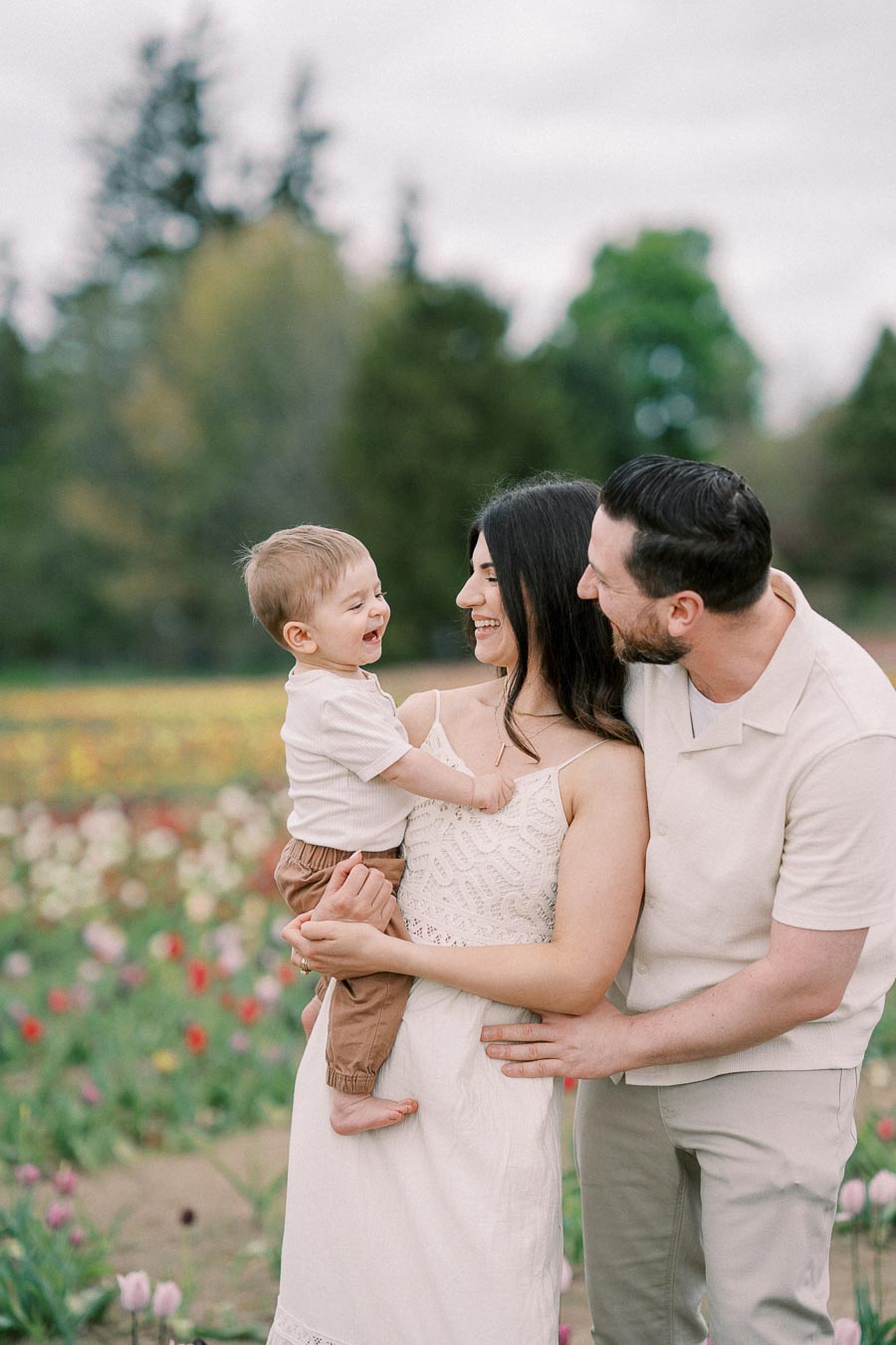 A joyful family moment captured in a vibrant tulip field, with the parents and their child sharing smiles and laughter.