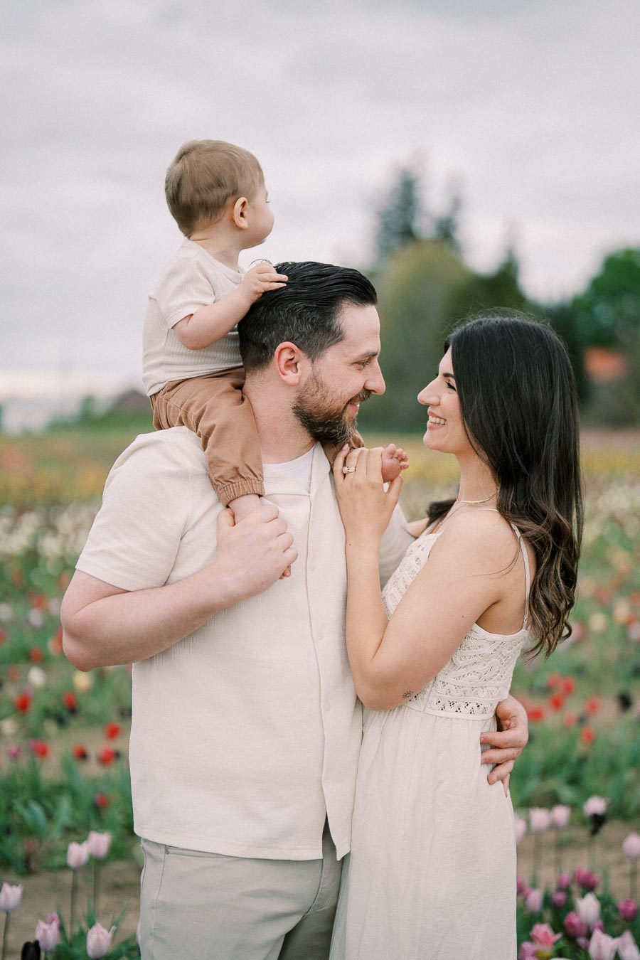 A joyful family moment captured in a tulip field, with a man holding a child on his shoulders and a woman smiling at them.