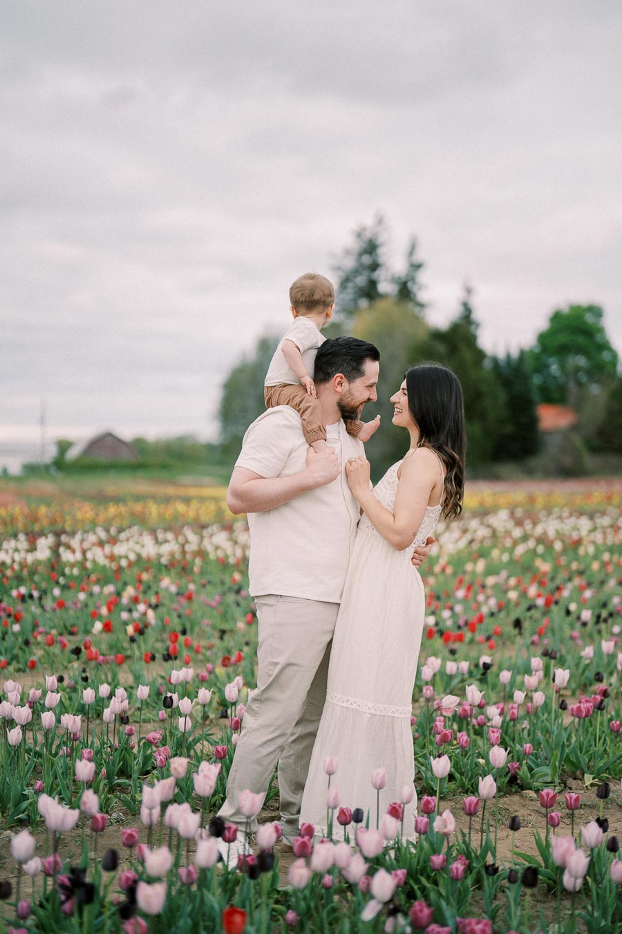 A family enjoys a moment together in a vibrant tulip field, with the father carrying their child on his shoulders while the mother smiles at them.