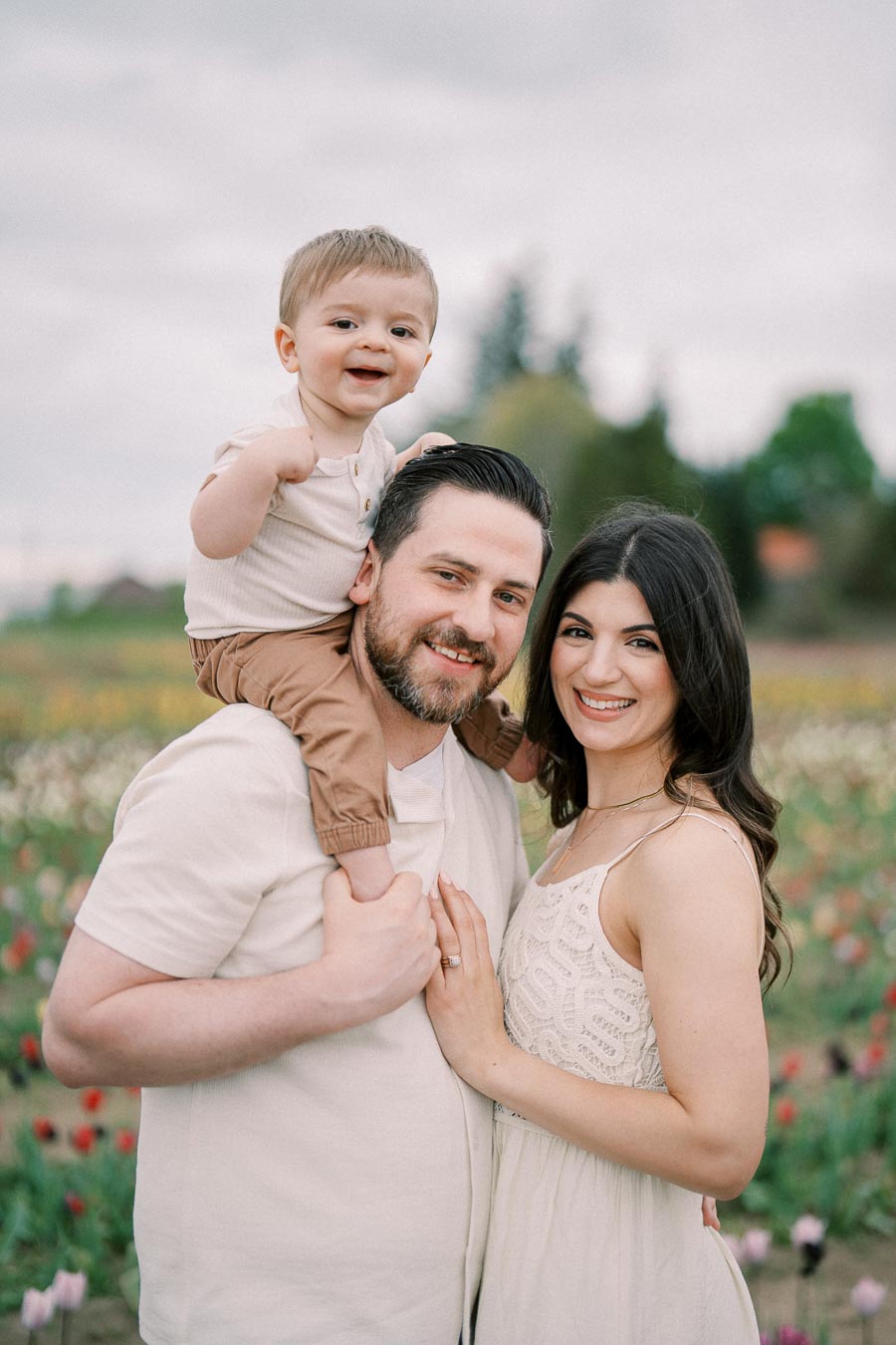 A happy family enjoying a day in a tulip field, with the father carrying their child on his shoulders and the mother standing beside them.
