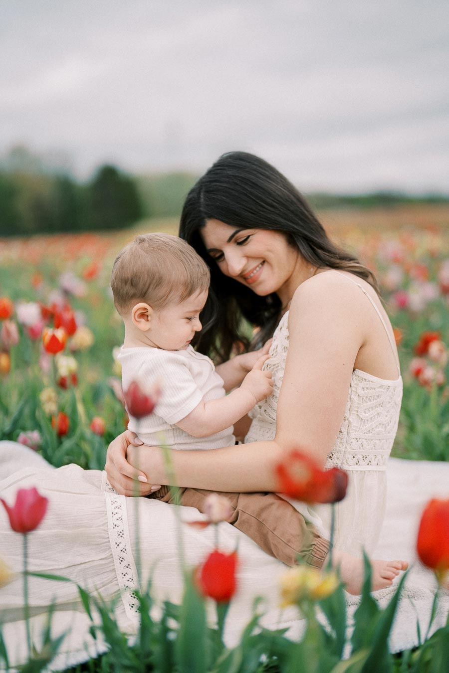 A woman lovingly holds a baby while sitting in a vibrant field of tulips, creating a serene and joyful scene.