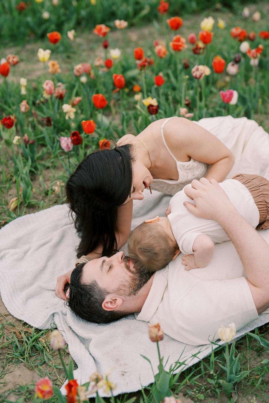 A family enjoys a peaceful moment lying on a blanket amidst a vibrant field of tulips.