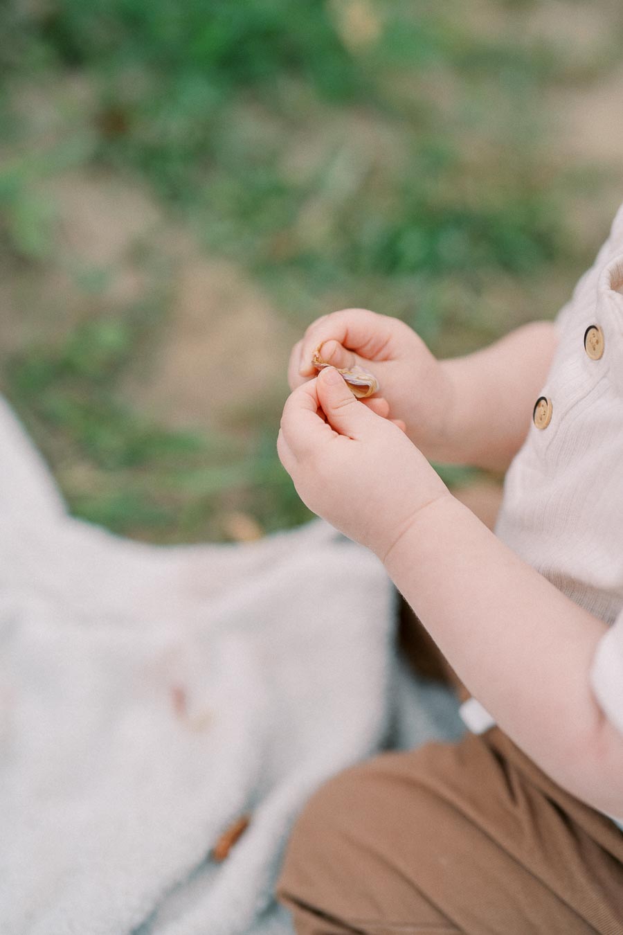 A child holding a small object while sitting outdoors on a blanket.