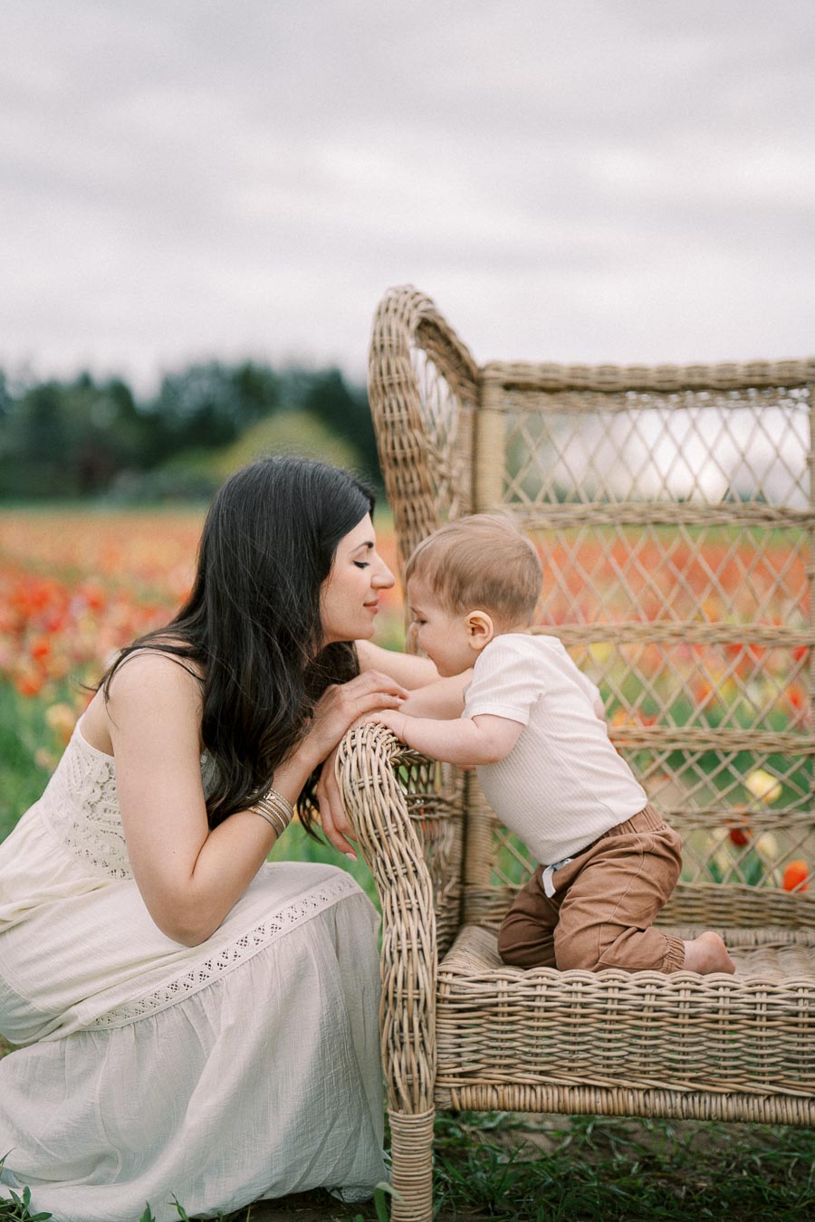 A tender moment between a woman and a baby on a wicker chair in a vibrant flower field.