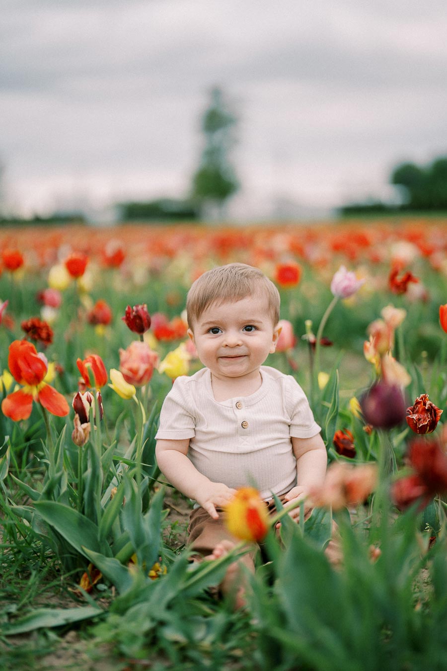 A cheerful baby sits among vibrant tulips in a field, enjoying a serene moment in nature.
