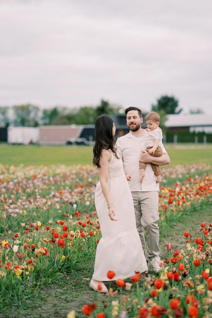 A family enjoys a day out in a vibrant tulip field, with the father holding their child and the mother smiling at them.