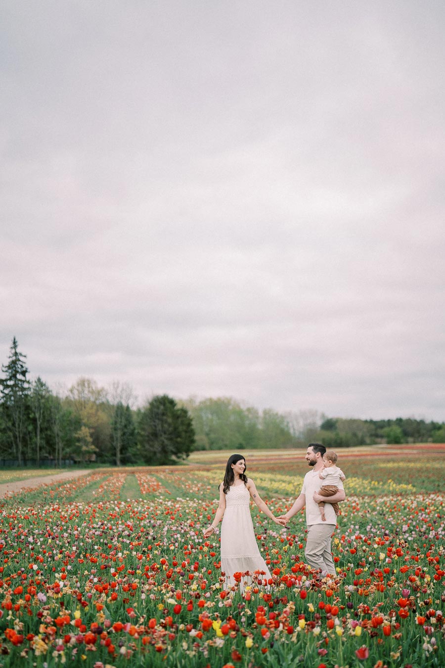 A family enjoys a stroll through a vibrant tulip field, surrounded by colorful blooms under a cloudy sky.