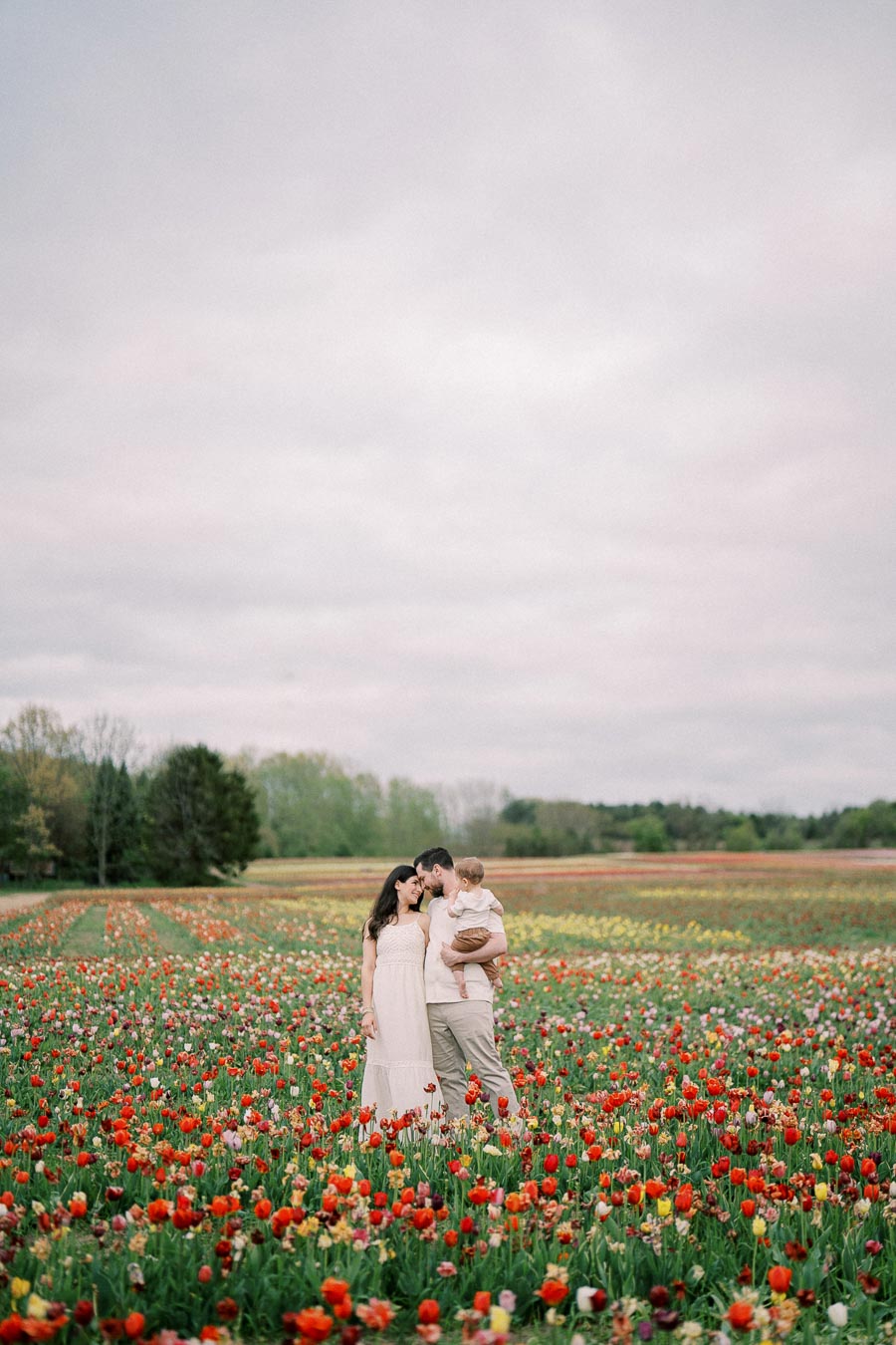 A family enjoys a peaceful moment in a vibrant tulip field, surrounded by a sea of colorful flowers under an overcast sky.