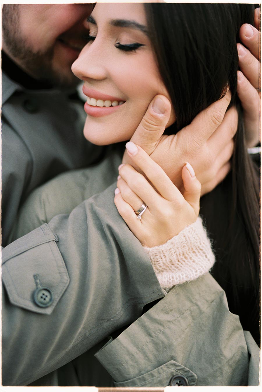 A close-up of a couple embracing, highlighting the woman's smile and engagement ring.