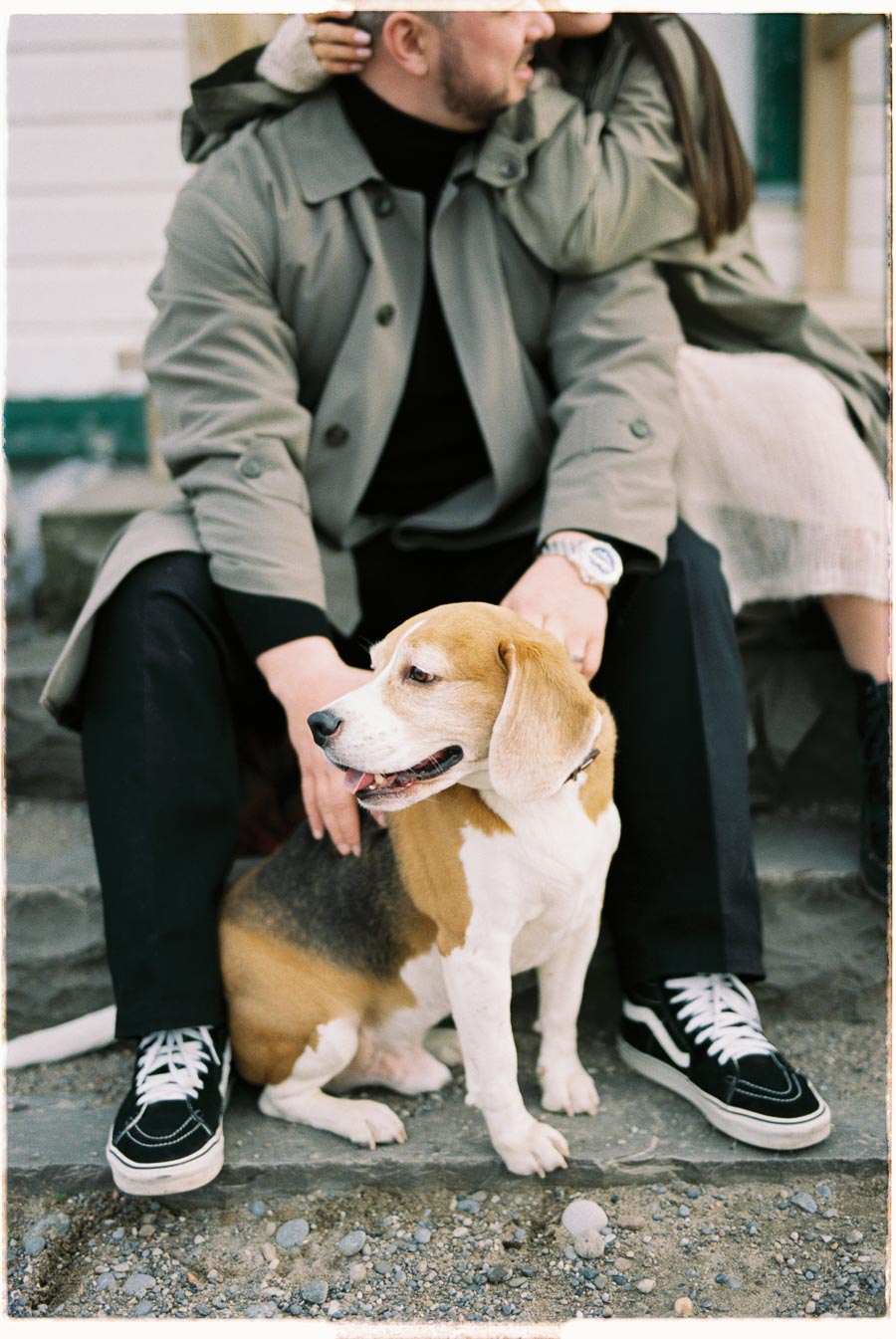 A couple sits on steps with a beagle dog in front of them, enjoying a relaxed moment outdoors.