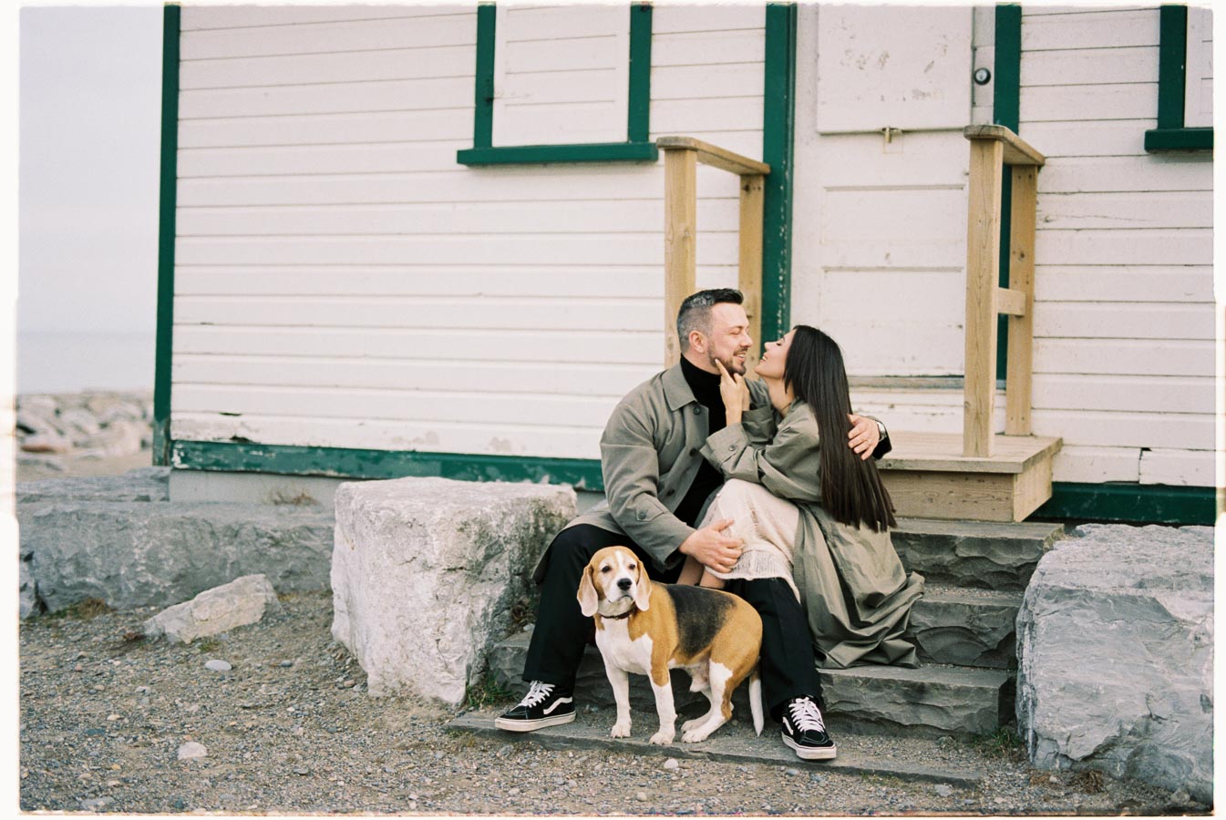 A couple shares a tender moment on the steps of a rustic building, accompanied by their beagle.