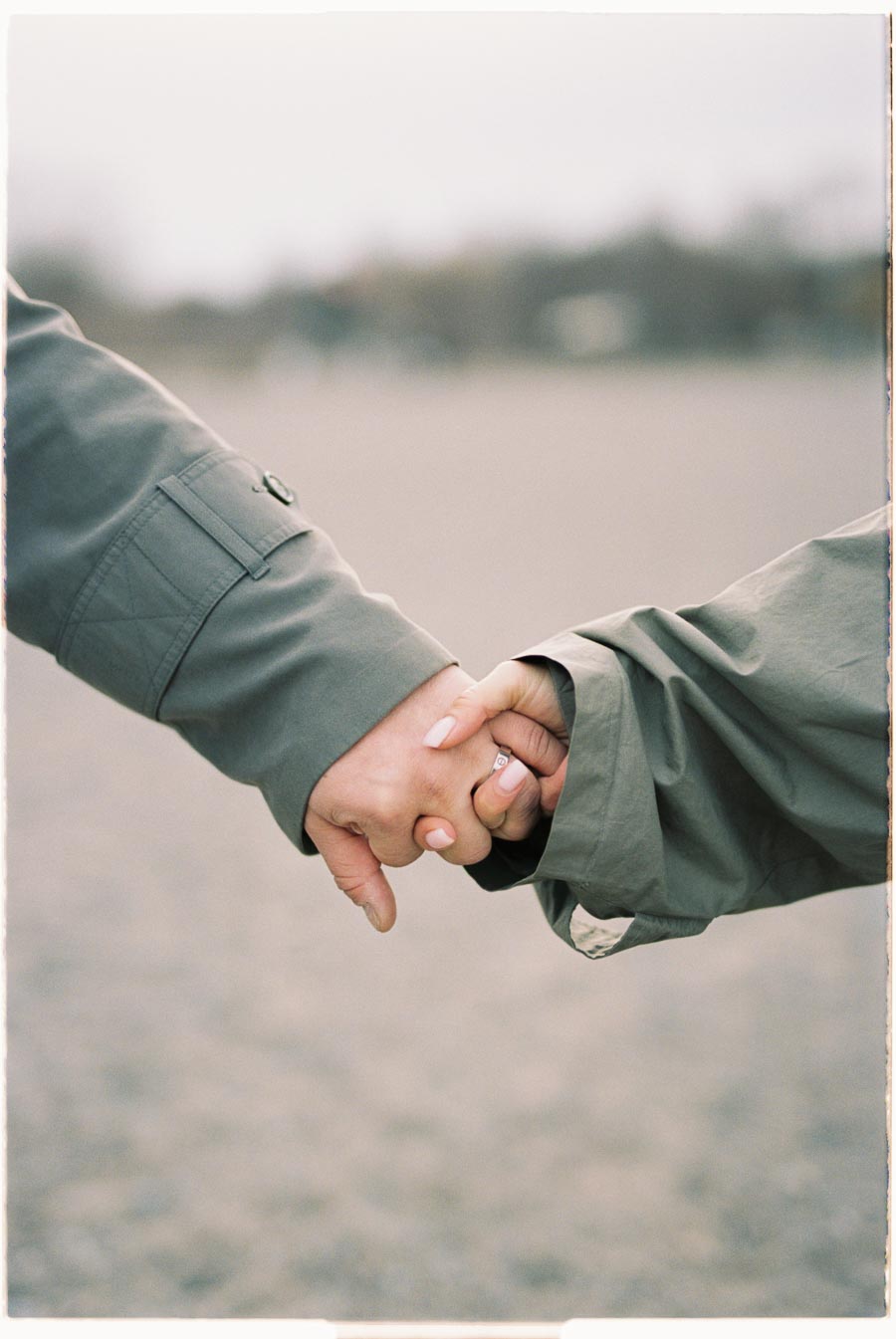 Two individuals hold hands, each wearing a jacket, symbolizing connection and togetherness in an outdoor setting.