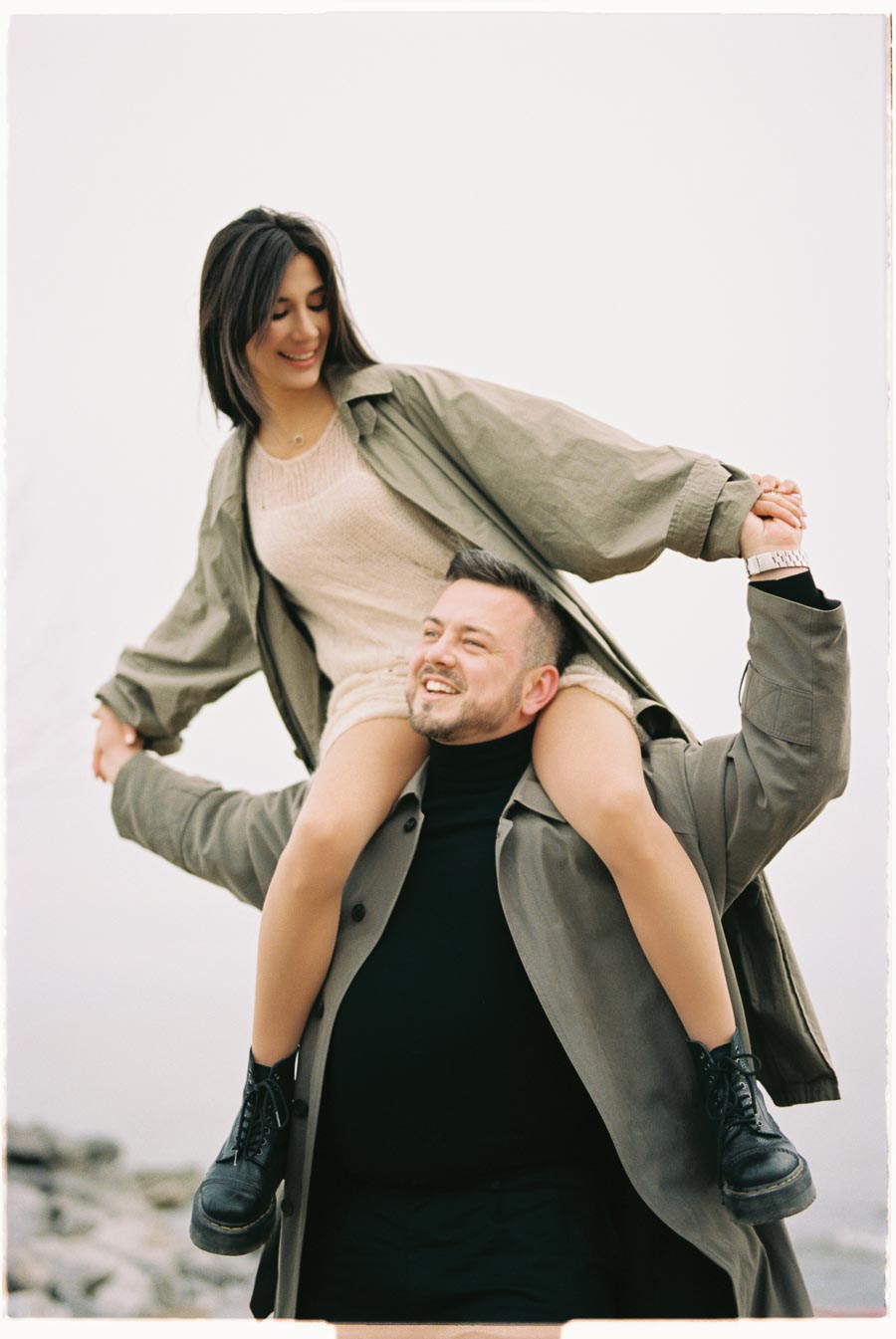 A joyful moment captured as a woman sits on a man's shoulders, both dressed in casual attire and smiling.