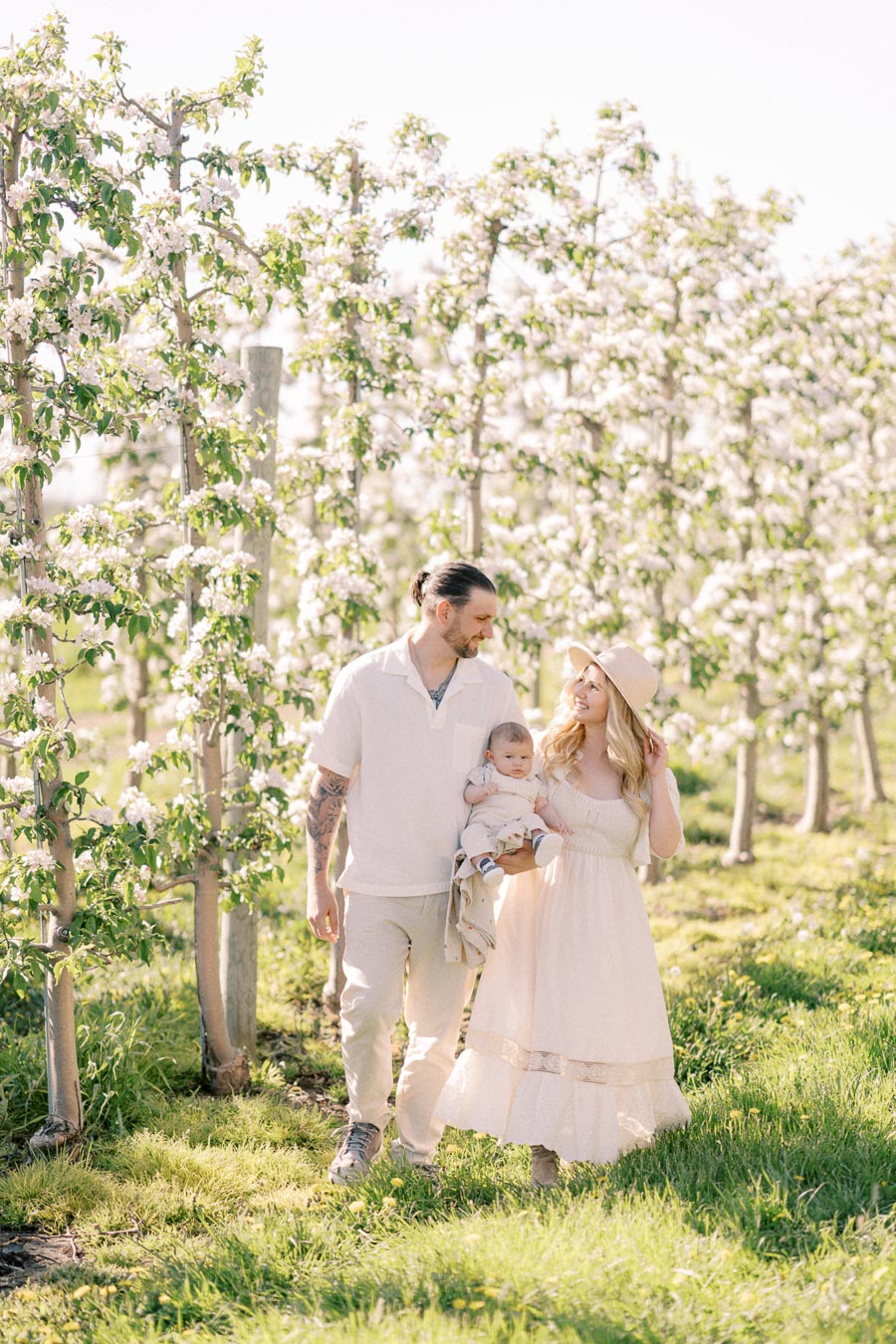 A family enjoys a sunny day walking through a blooming orchard, surrounded by lush greenery and flowering trees.