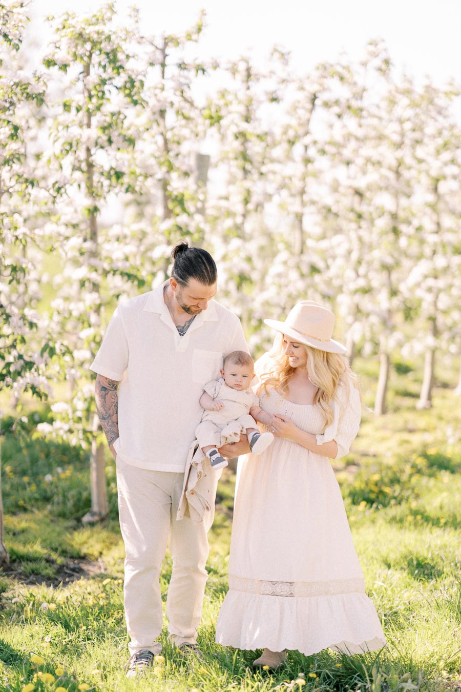 A family enjoys a sunny day in a blooming orchard, dressed in light, coordinated outfits.