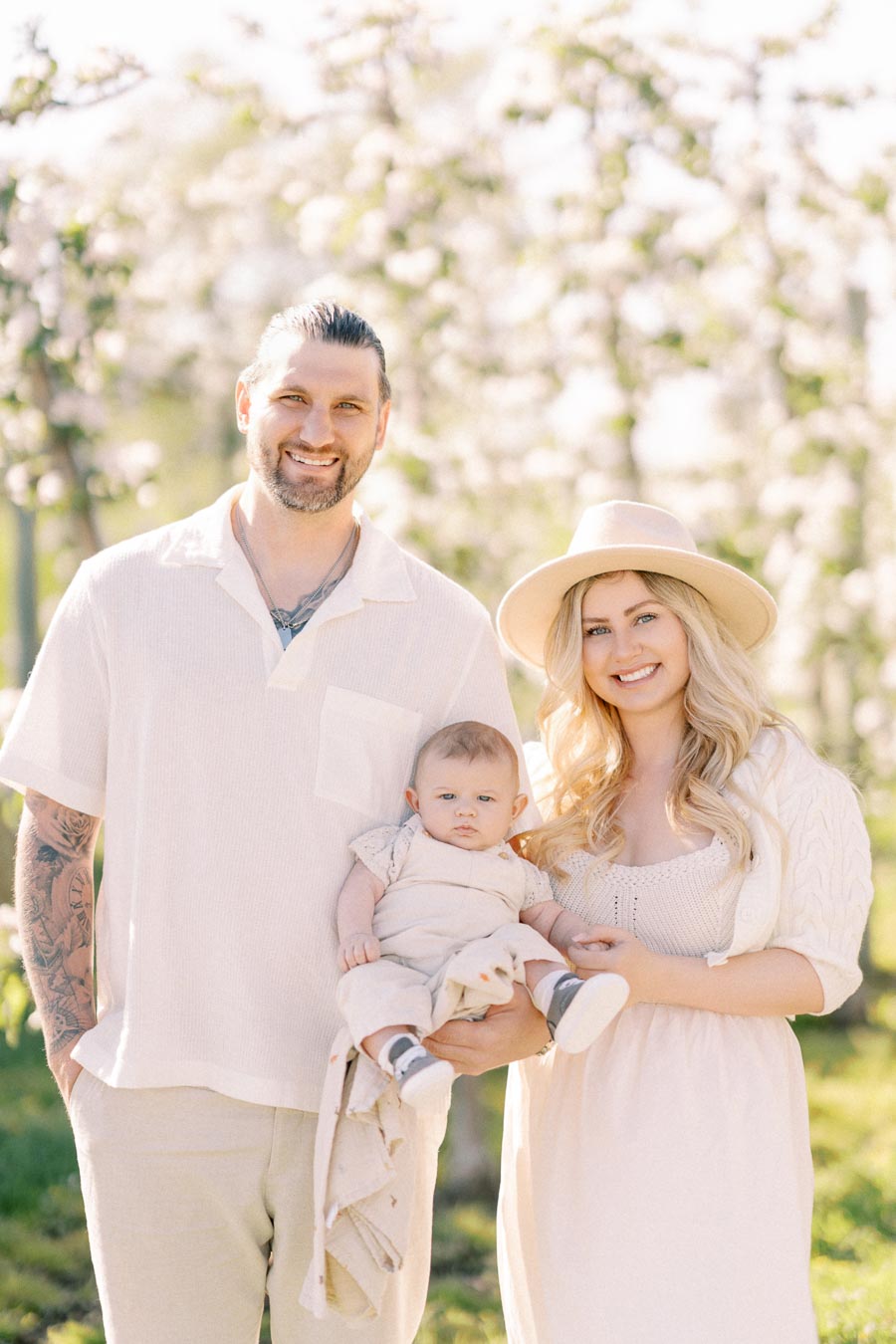A family enjoying a sunny day in a garden with blooming trees, dressed in light-colored clothing.