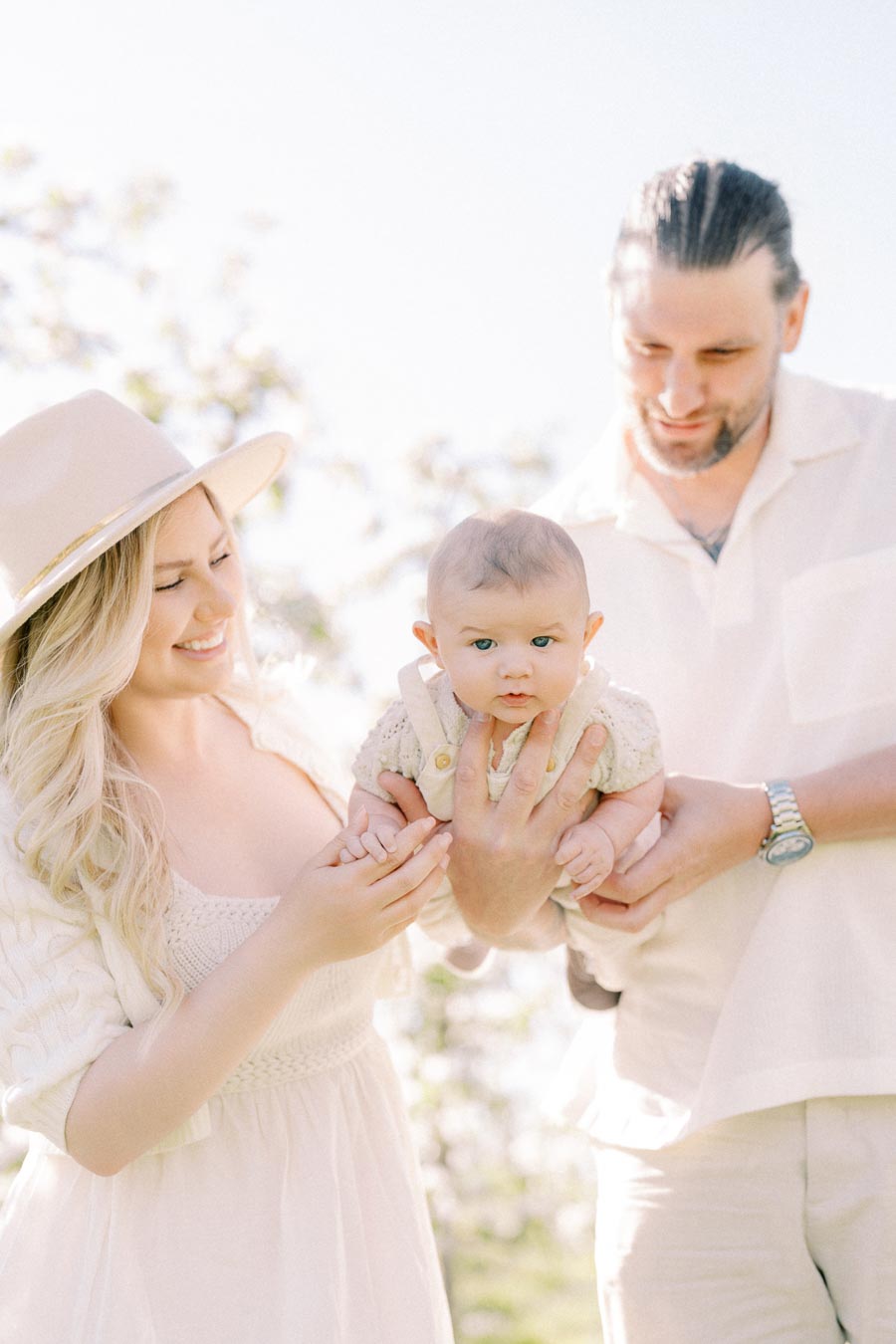 A joyful couple holding their baby outdoors, enjoying a sunny day.