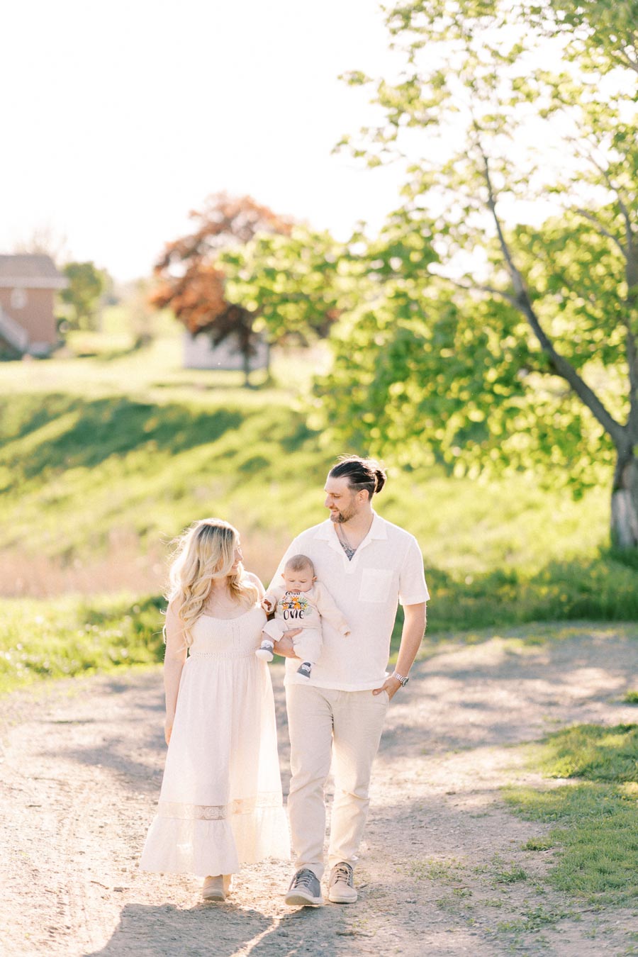 A family enjoys a sunny day in the park, walking along a dirt path surrounded by lush greenery.