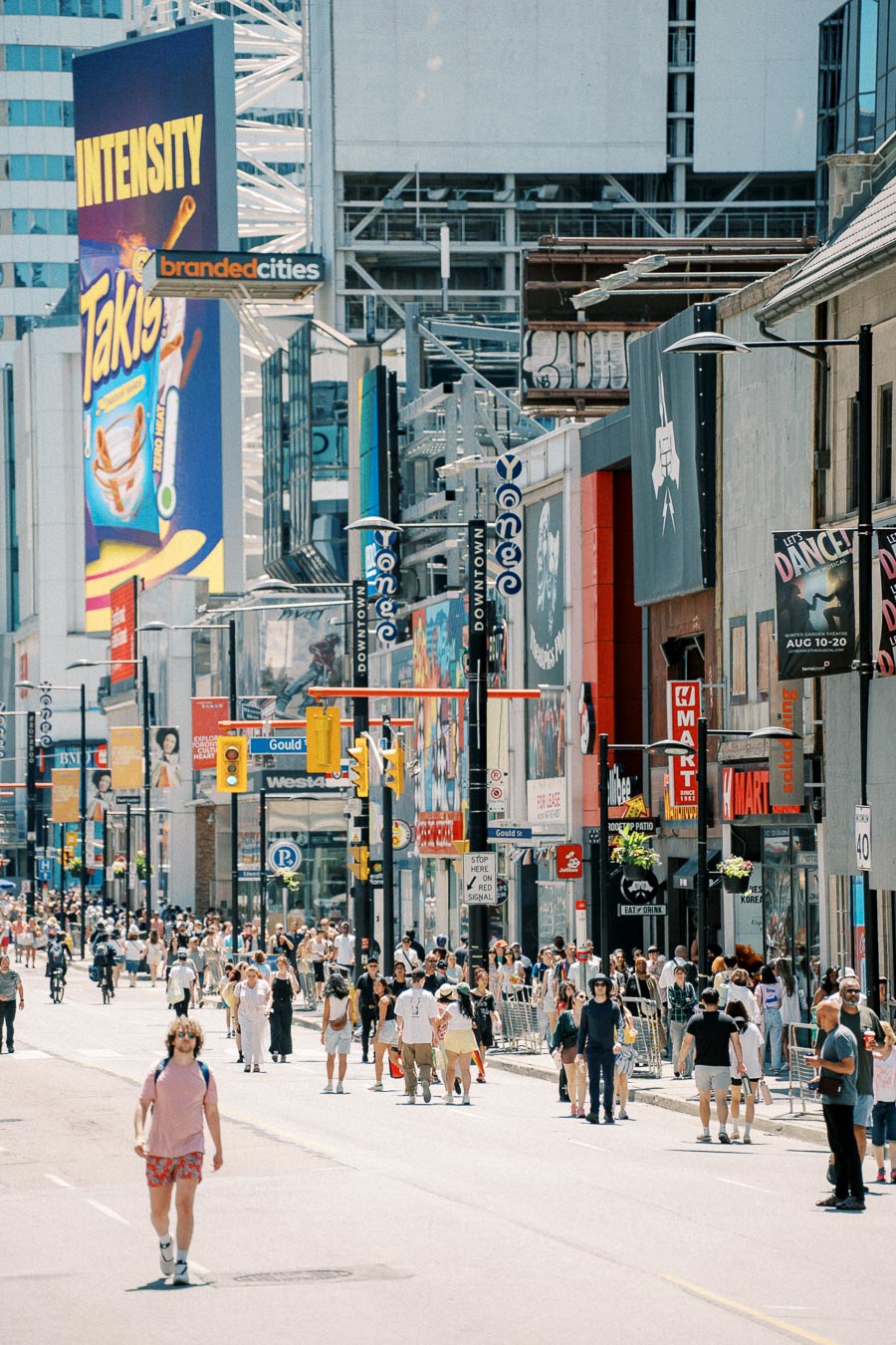 A bustling city street scene with pedestrians and large advertisements on buildings, including a prominent Takis ad.