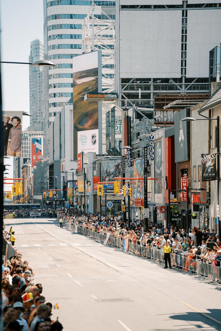 Crowds gather along a city street lined with tall buildings, possibly for a parade or public event.
