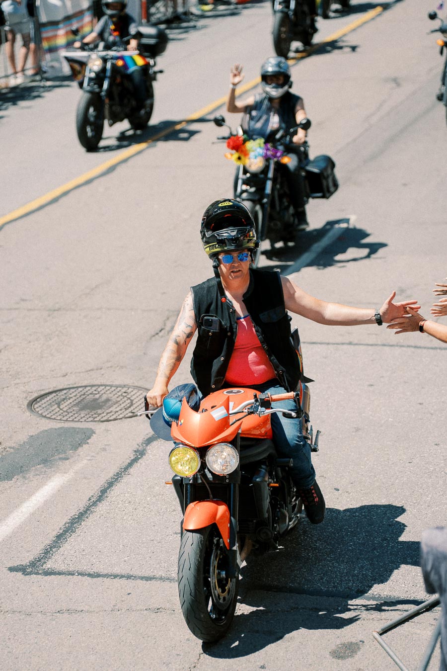 A motorcyclist participates in a parade, engaging with the crowd while riding an orange motorcycle.
