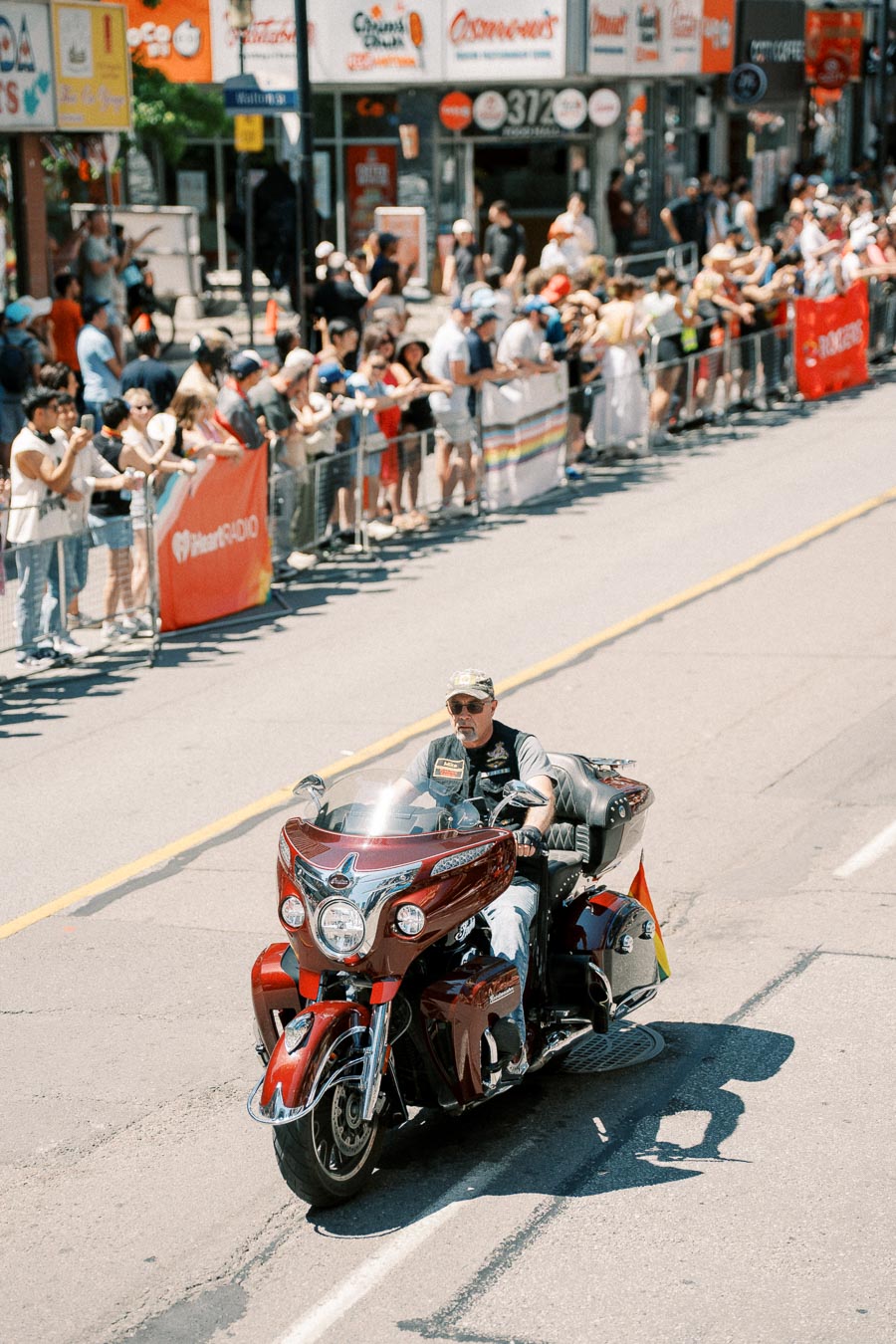 A man rides a red motorcycle during a parade, with spectators lining the street.