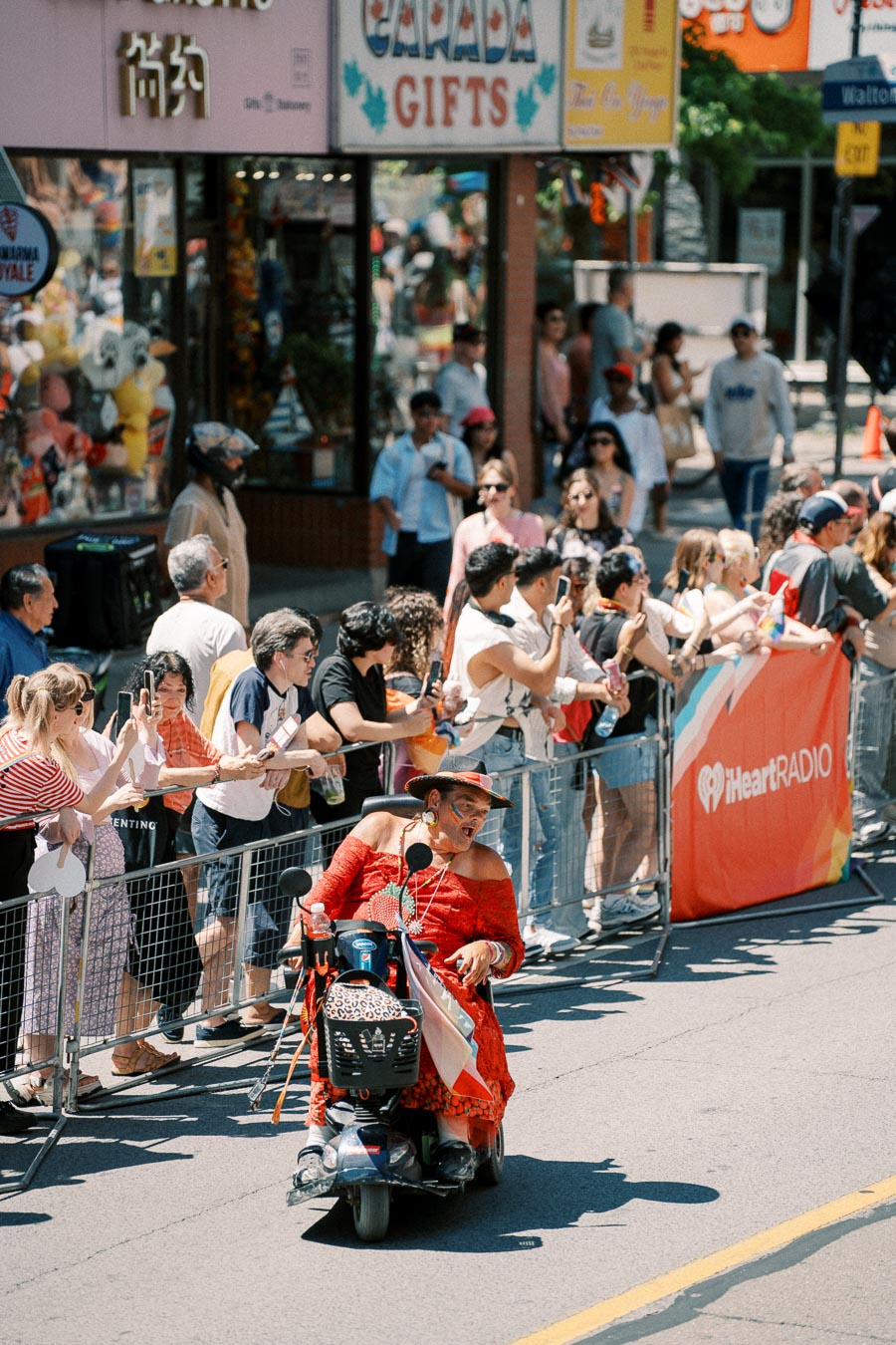 A vibrant parade scene with a person in a red outfit on a mobility scooter, engaging with an enthusiastic crowd.
