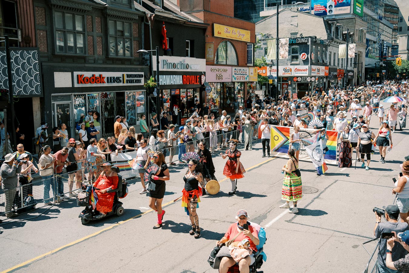 A lively parade with participants in colorful costumes and flags, drawing a large crowd on a city street.