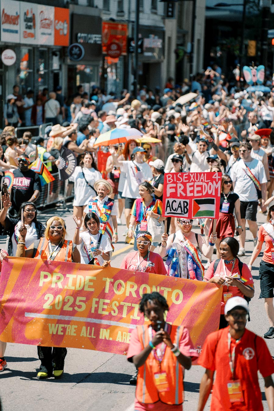 Participants at the Pride Toronto 2025 Festival parade, showcasing colorful banners and signs promoting LGBTQ+ rights and inclusivity.