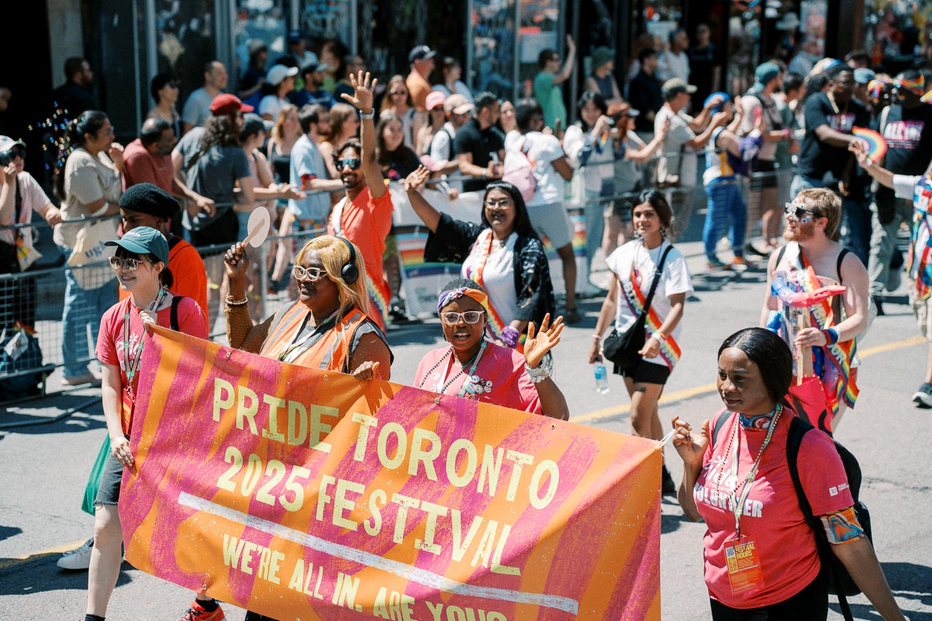 Participants in the Pride Toronto 2025 Festival parade hold a vibrant banner as they march down the street, surrounded by a lively crowd.