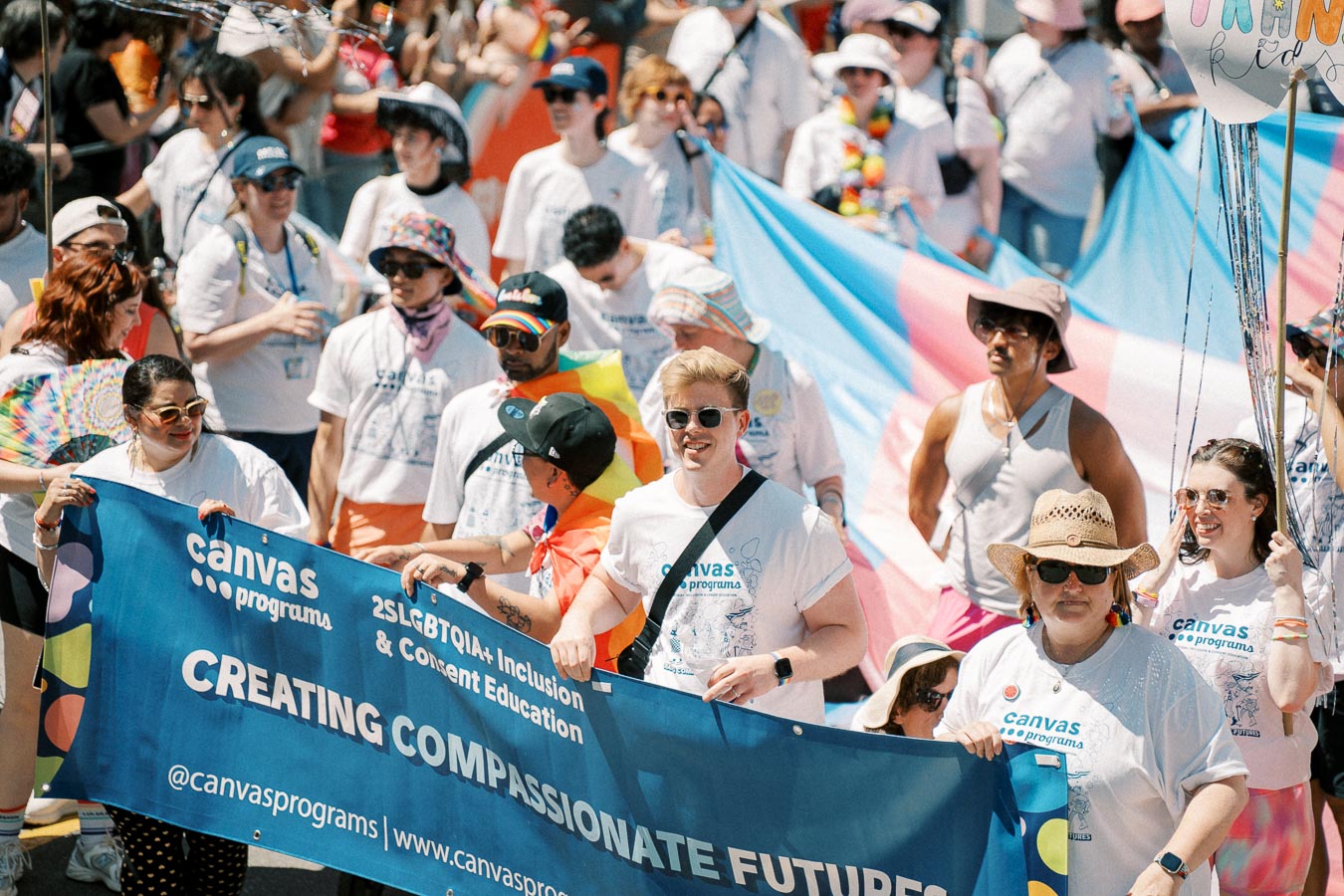 Participants in a pride parade hold a banner promoting 2SLGBTQIA+ inclusion and consent education.
