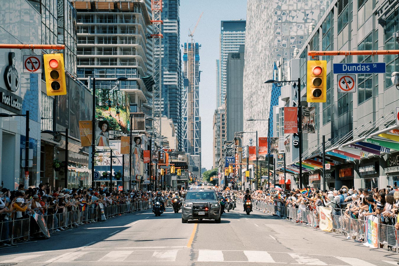 A parade on Dundas Street, Toronto, featuring police vehicles and a large crowd of spectators lining the street.