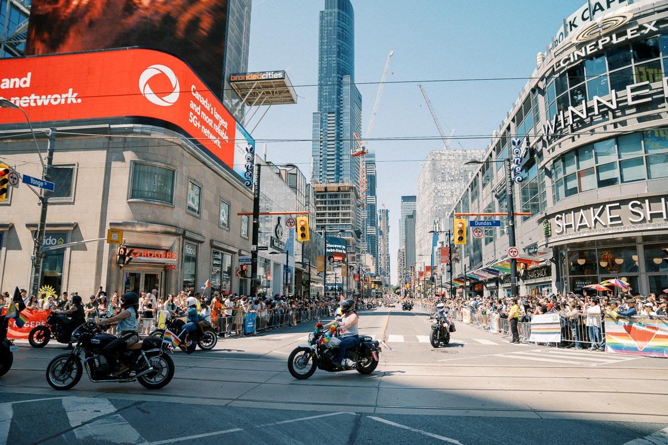 A vibrant parade on Yonge Street in Toronto, featuring motorcyclists and cheering crowds, set against the backdrop of tall city buildings.
