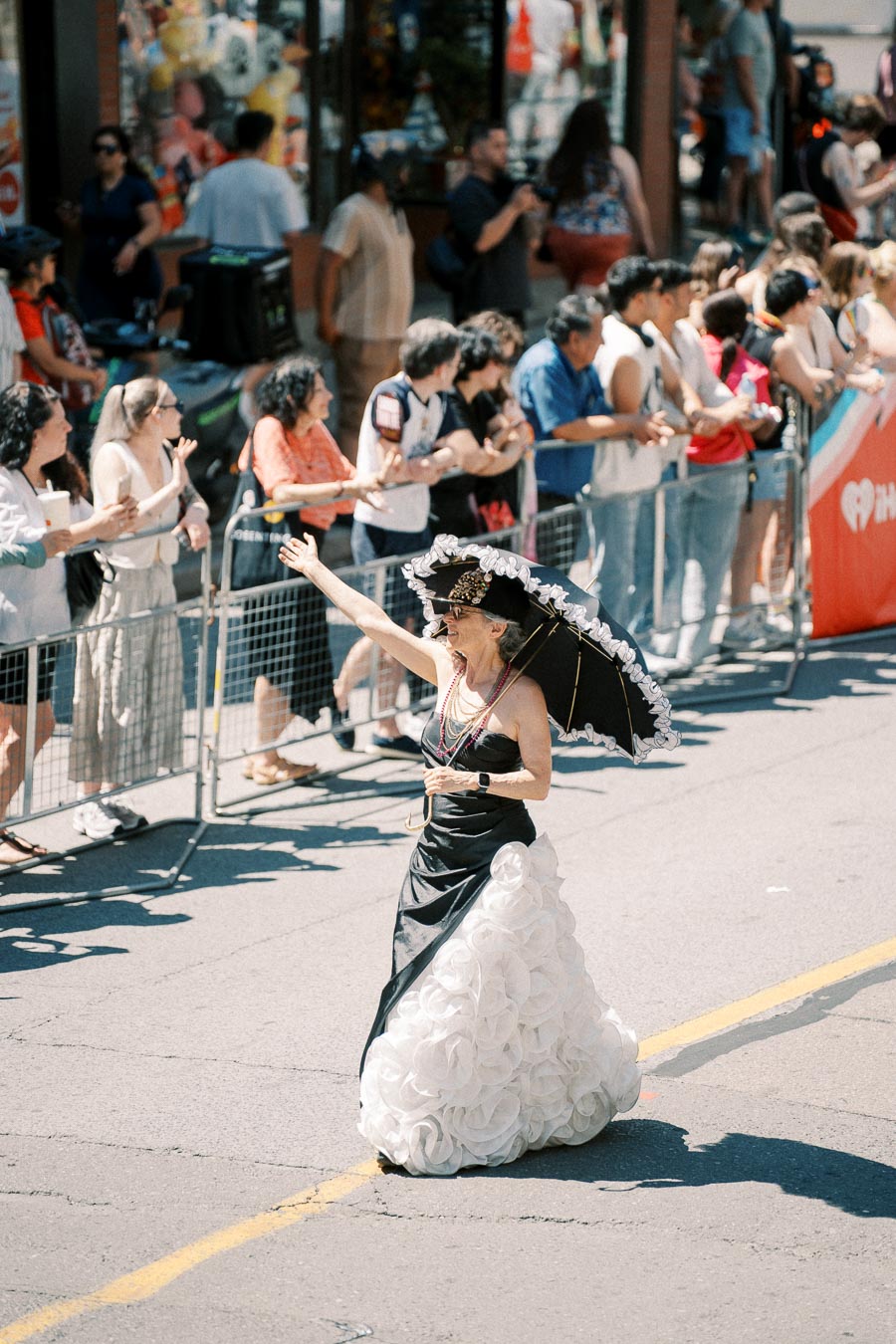 A parade participant in a striking black and white dress waves to the crowd, holding a matching parasol.