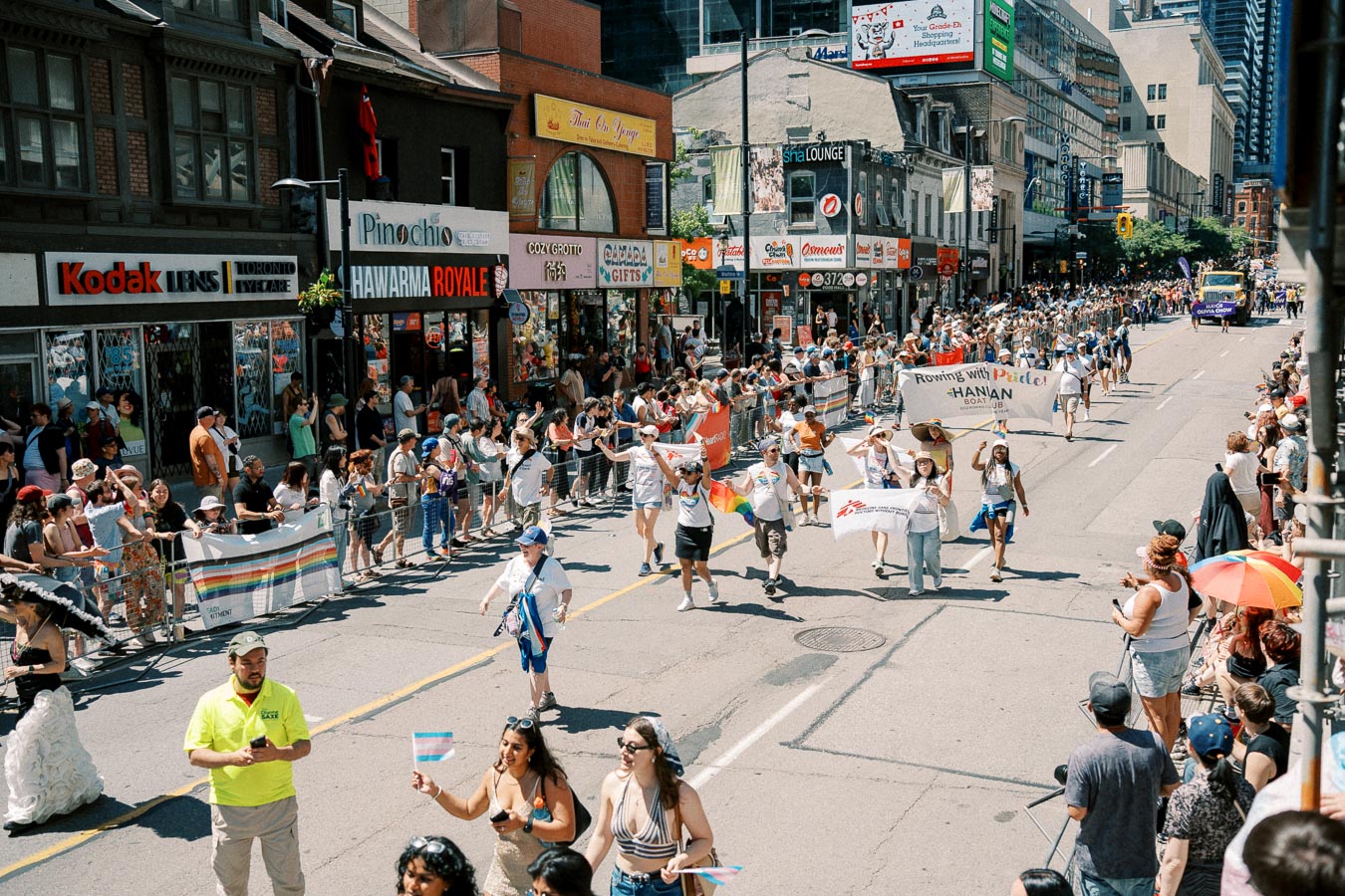 A lively parade takes place on a city street, with participants carrying banners and flags, while spectators line the sidewalks.