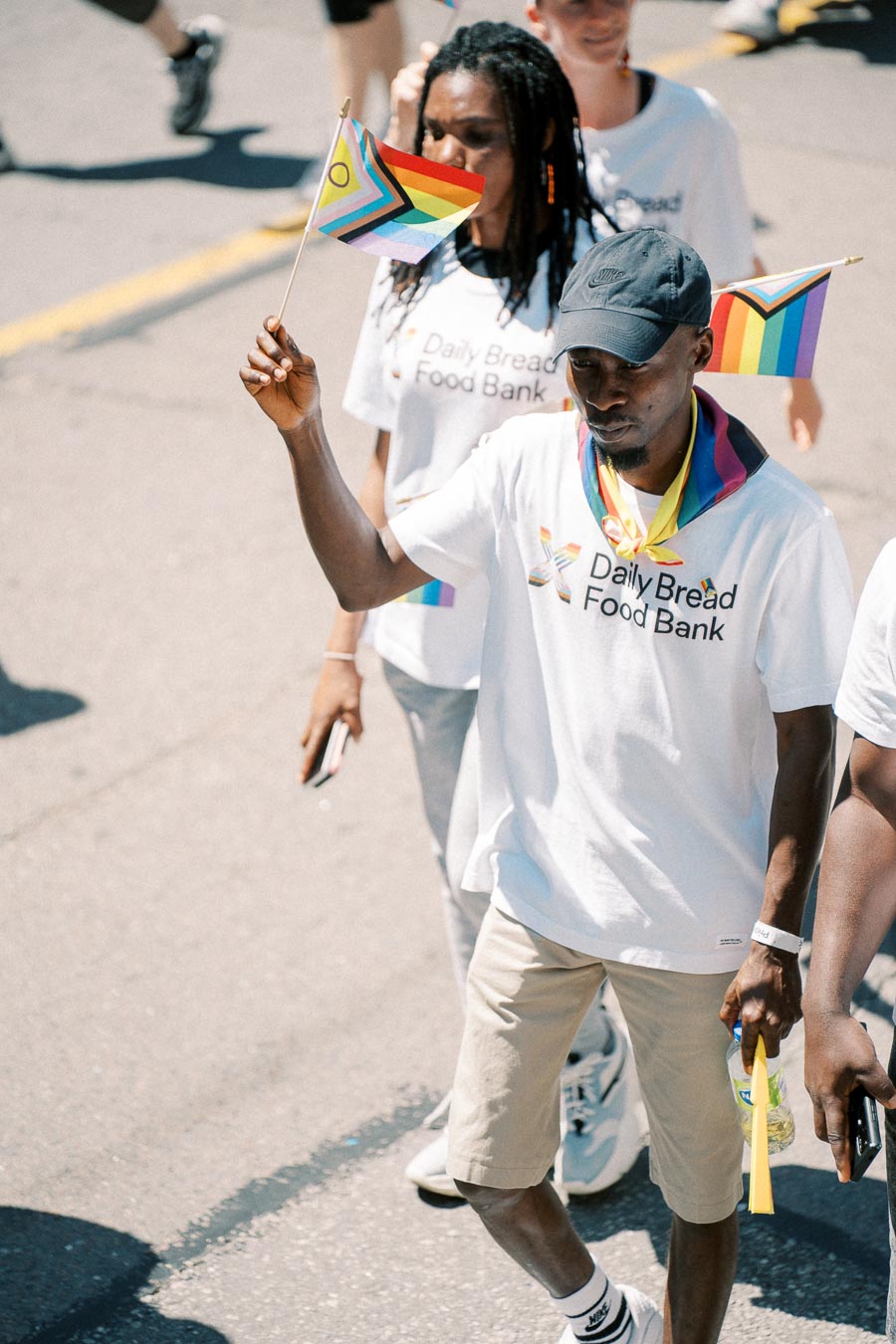 Participants in a parade wearing "Daily Bread Food Bank" t-shirts and holding pride flags.