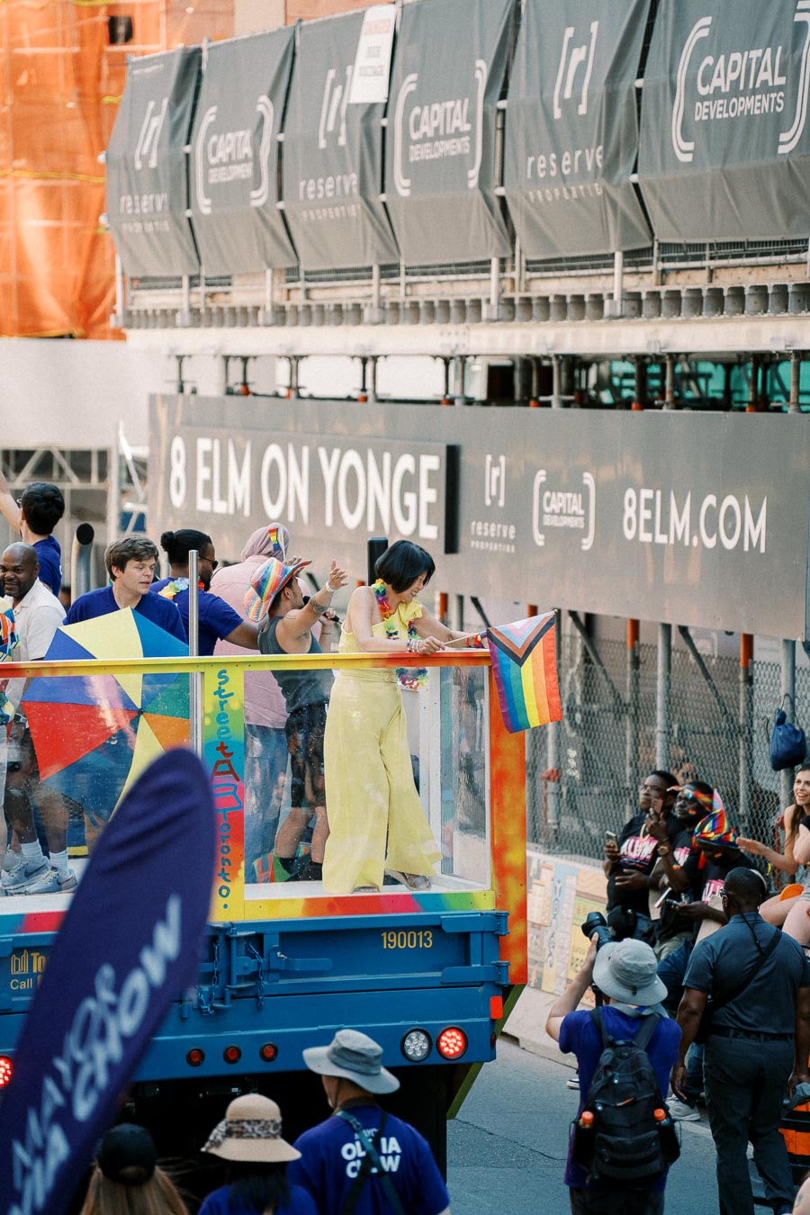 Participants on a colorful parade float celebrate at a pride event on Yonge Street, with rainbow flags and festive attire.