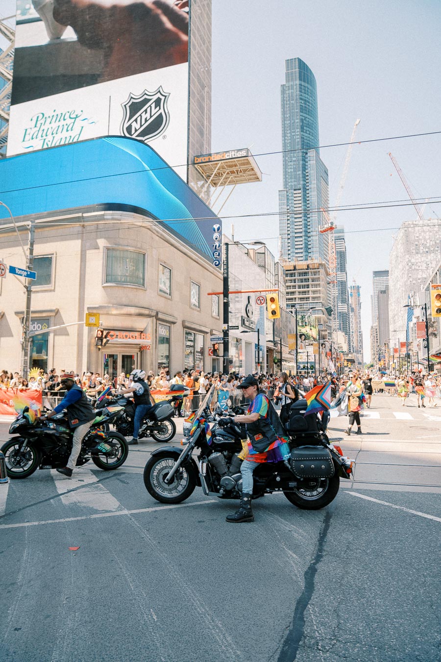 Motorcyclists participate in a city parade, surrounded by a crowd and skyscrapers.