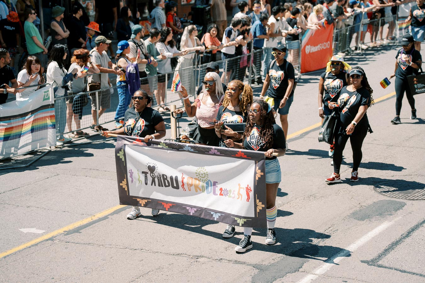 Participants march in a pride parade, holding a 'Tribu Pride 2023' banner, surrounded by a cheering crowd.