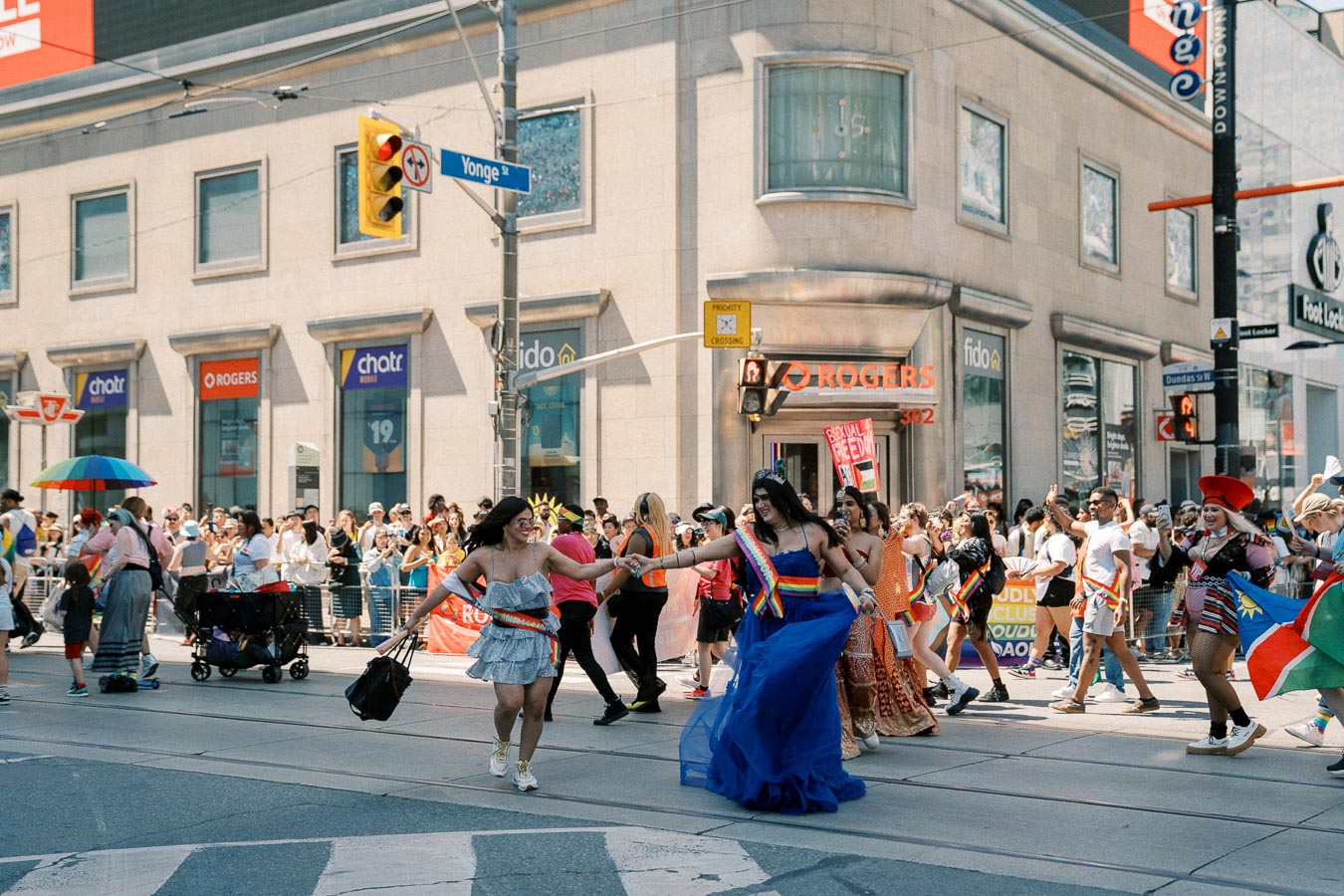 A lively parade celebrating diversity and inclusion takes place on a city street, with participants dressed in colorful outfits and rainbow accessories. Spectators line the sidewalks, enjoying the festive atmosphere.