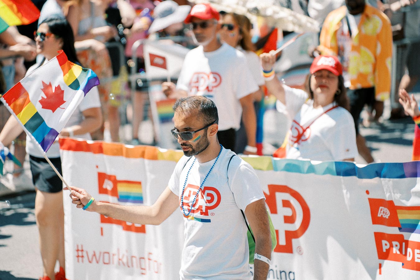 Participants in a pride parade hold a Canadian flag with rainbow colors, celebrating diversity and inclusion.