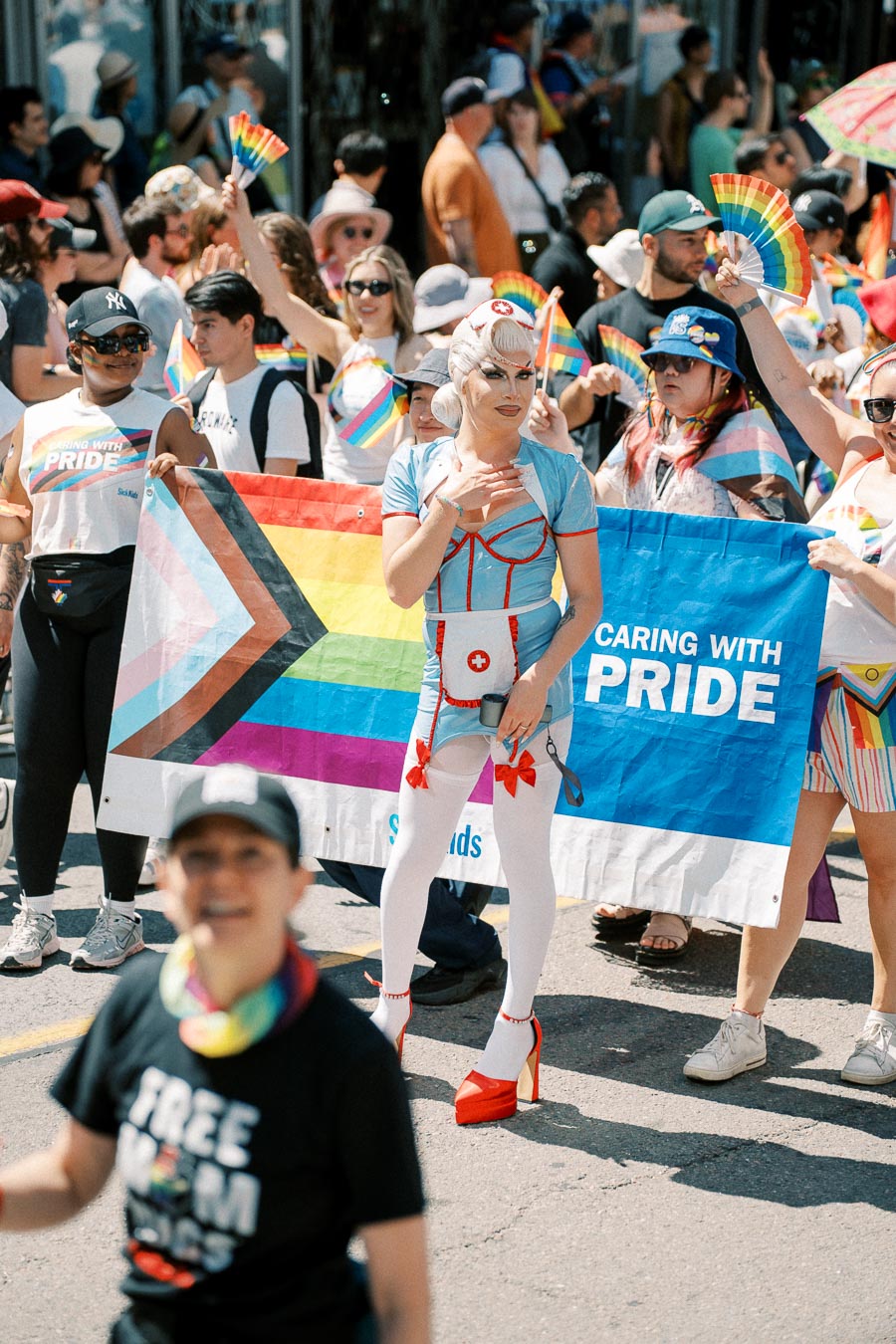 Participants in a Pride parade hold a colorful banner with the message 'Caring with Pride'.