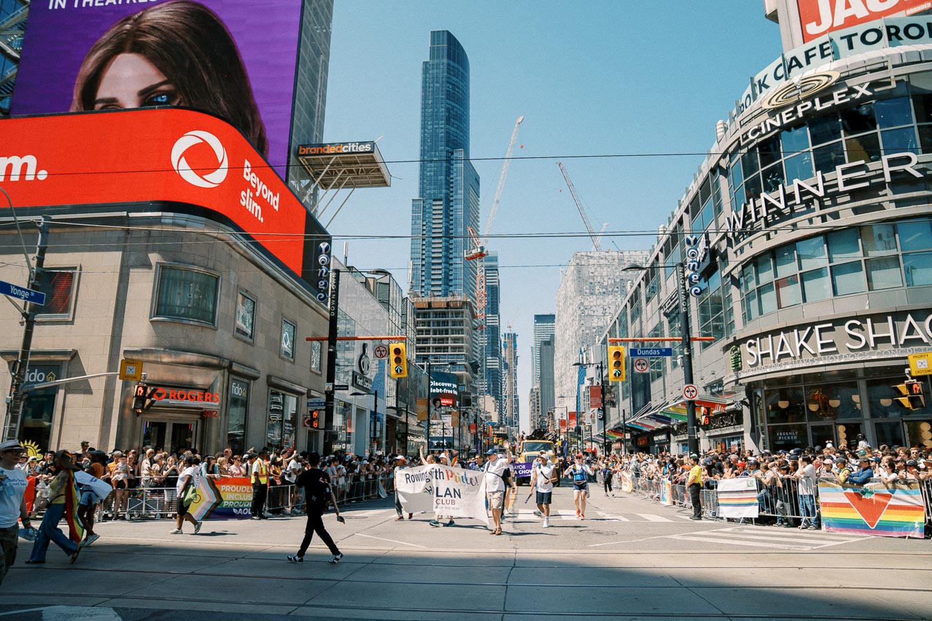 A vibrant parade at Yonge-Dundas Square in Toronto, with crowds and participants celebrating amidst the city's iconic billboards and skyscrapers.