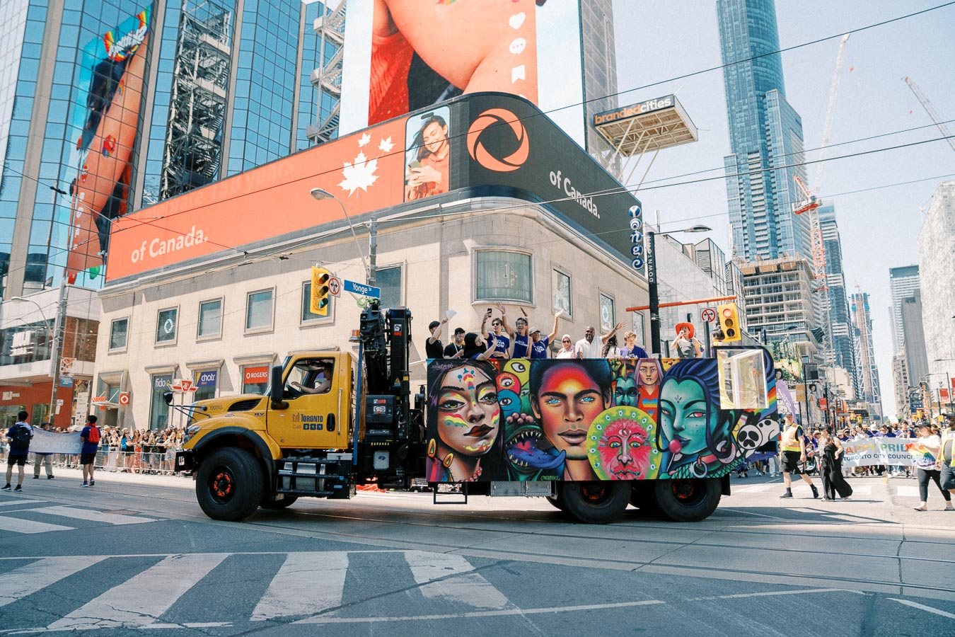 A vibrant parade float with colorful artwork travels through a city street, surrounded by skyscrapers and large digital billboards.