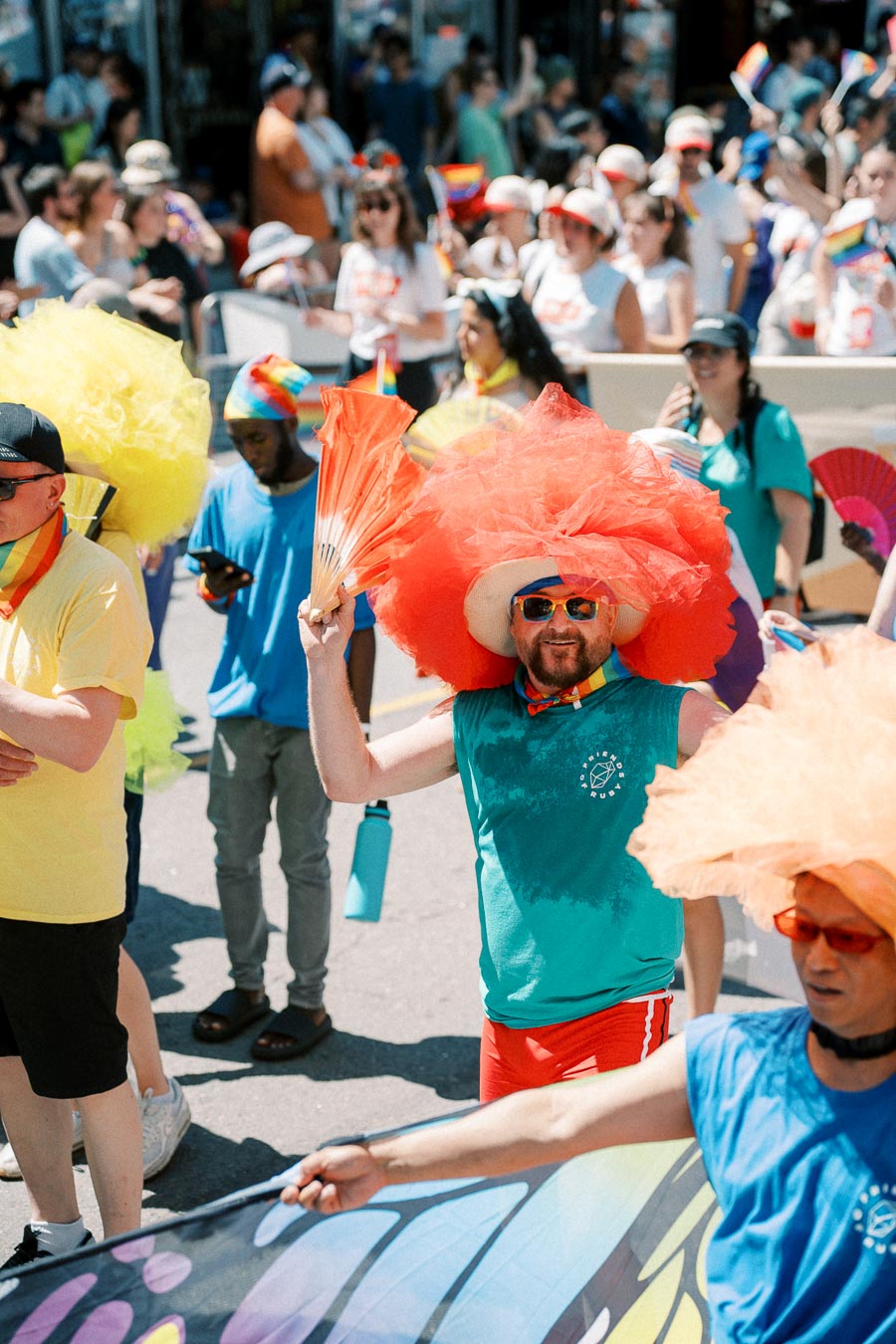 Participants in a colorful parade wearing vibrant outfits and accessories, celebrating with fans and hats.