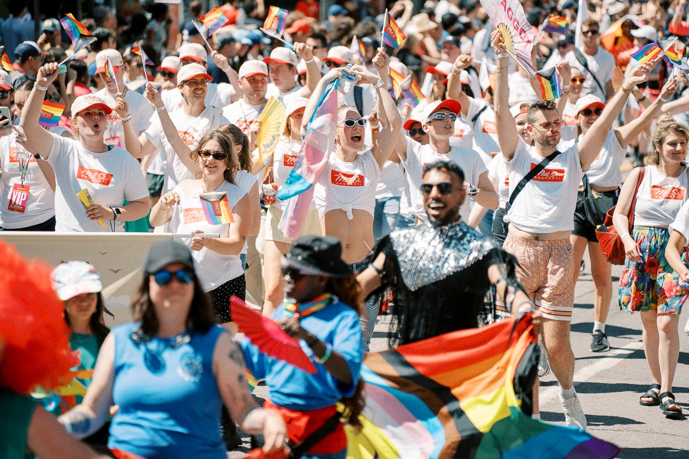 Participants in a pride parade celebrate with rainbow flags and festive attire, showcasing support for the LGBTQ+ community.